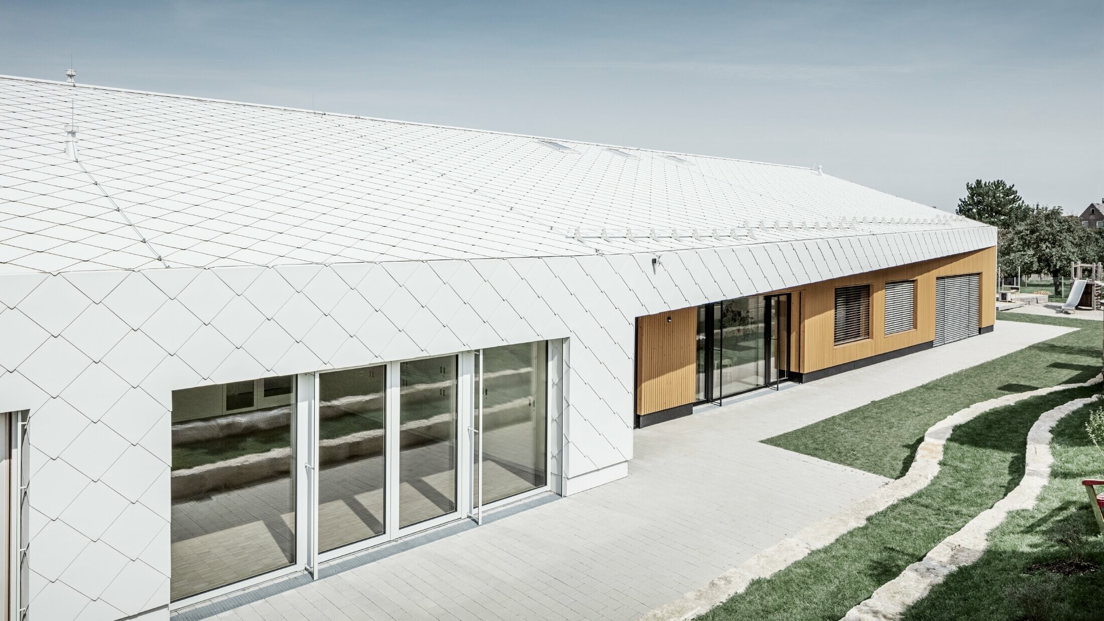 Förskola täckt med PREFA tak- och väggromb 44 i prefavit, takytan sträcker sig vidare ut över fasaden; stora fönsterytor