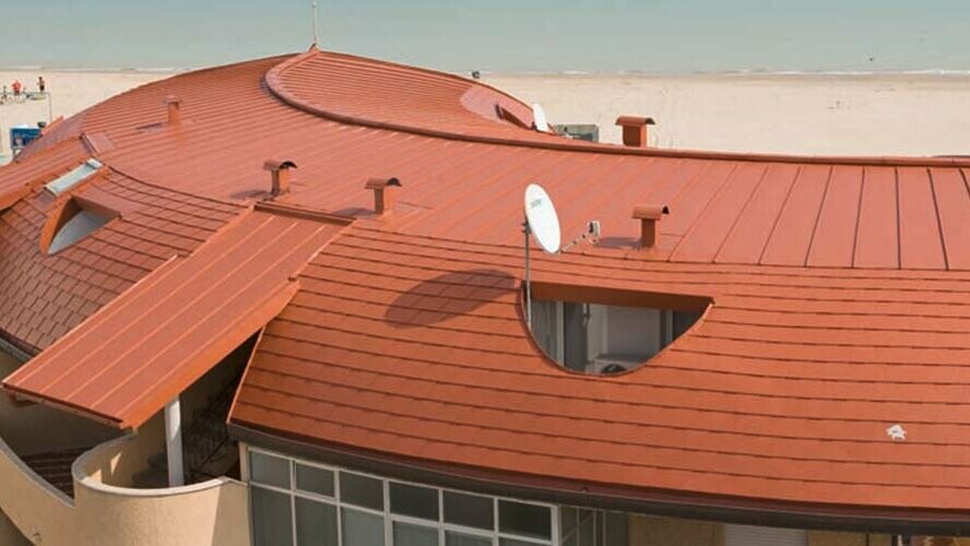 Rundat tak på en bostadshusanläggning, täckt med PREFA-takplattor, samt stående falstak – Prefalz – från PREFA i tegelrött.