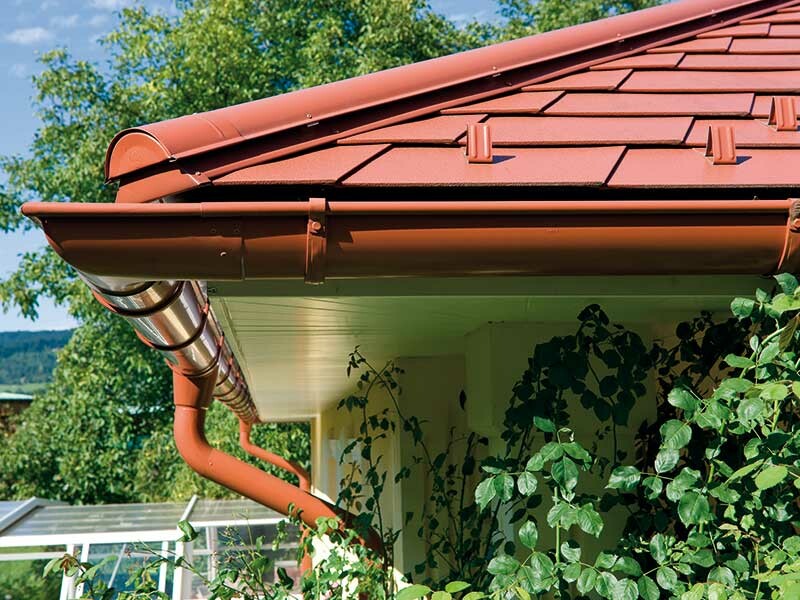 Detaljbild av PREFA-takplattan i tegelrött med matchande takränna, också i tegelrött.