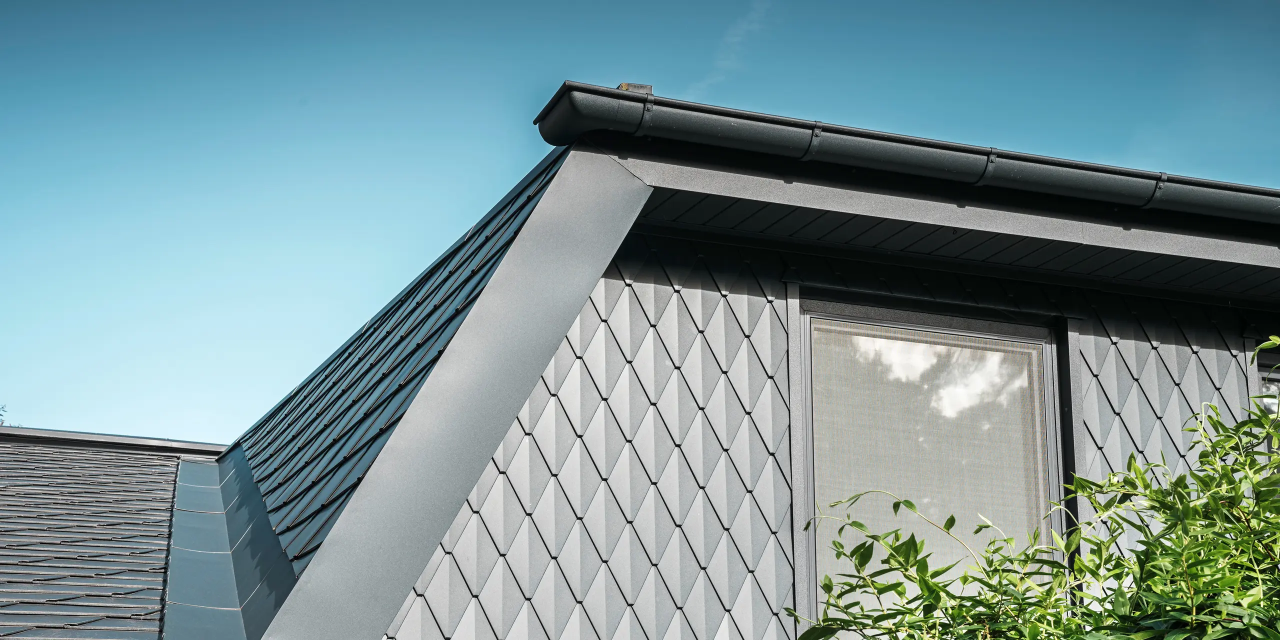 Trapezgaube på en enfamiljsvilla i Mechernich, klädd med små PREFA takplattor i P.10 antracit. Taket är täckt med PREFA takplattor DS.19 i samma färg. Den högkvalitativa aluminiumklädseln garanterar väderbeständighet och ett modernt, estetiskt utseende.