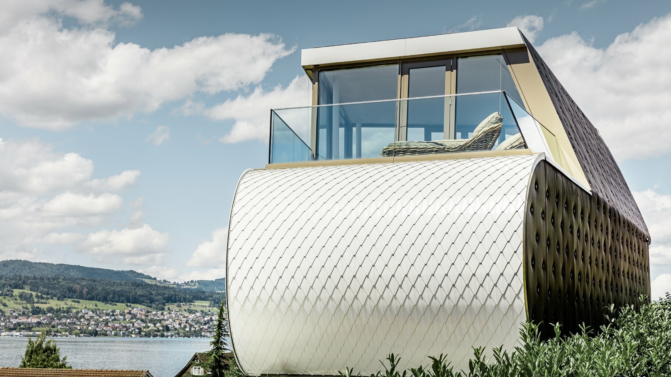 Vy från sidan på det enastående Flexhouse, ritat av Camenzind Architekten AG; man ser en av de svängda ytterväggarna som är täckt med en aluminiumfasad med PREFA i renvit som liknar fiskfjäll.
