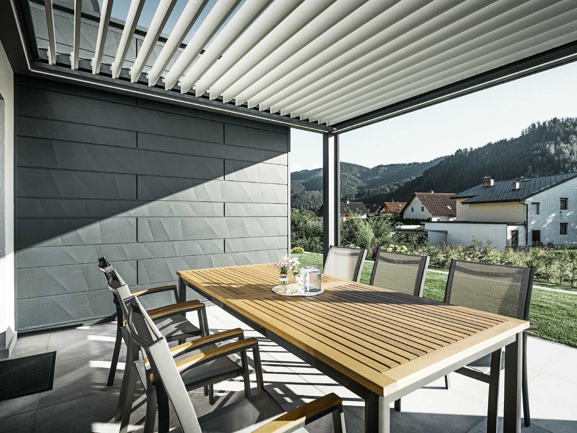 Mit Lamellen überdachte, geschützte Tersasse mit Tisch und Sesseln; eine Fassadenseite ist mit den PREFA Siding.X Fassadenpaneelen in Anthrazit verkleidet.