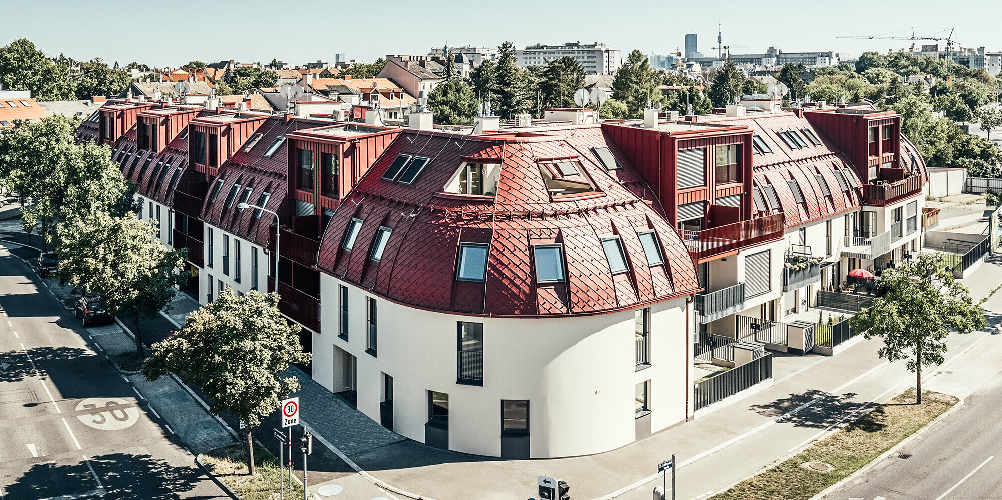 Straßenansicht auf die Wohnanlage Schöneck 13 und die abgerundete Dachlandschaft, entworfen vom Architekturbüro schneider+schumacher.