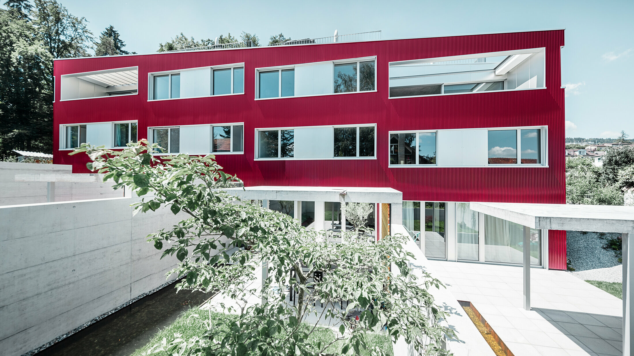 Bostadshus med flackt tak och balkong med vinröd fasad med PREFA vågprofil 