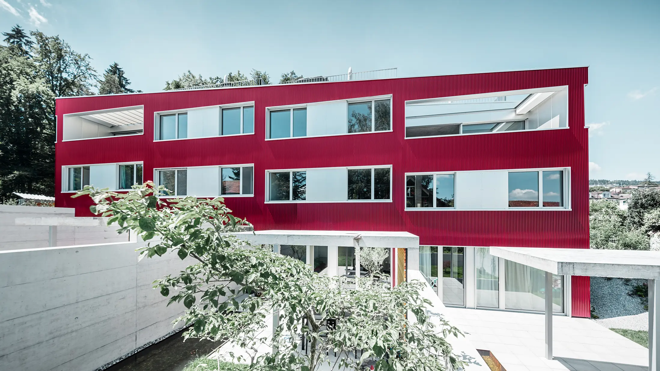 Bostadshus med flackt tak och balkong med vinröd fasad med PREFA vågprofil 