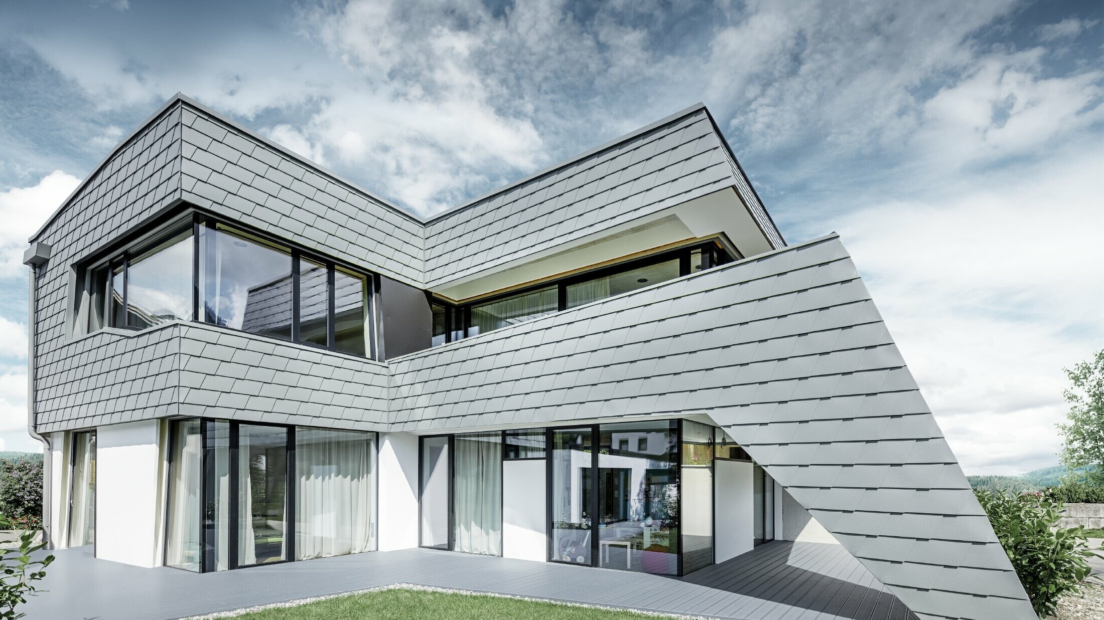 Modernt enfamiljshus med plantak, stora fönsterytor och en ljusgrå shingelfasad av aluminium från PREFA