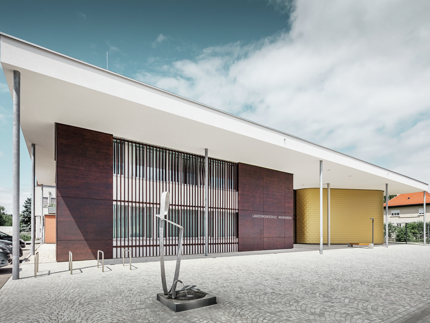 Außenaufnahme der Landesmusikschule in Buchkirchen. Das Gebäude trägt eine 160 m² große Fassade aus PREFA Wandschindeln in der Sonderfarbe Mayagold.