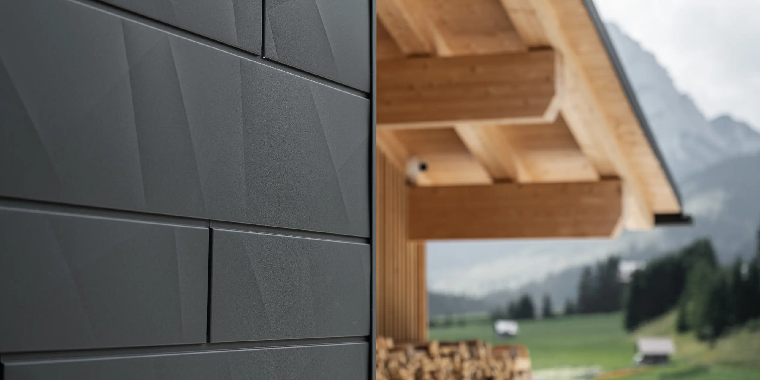 Närbild av Siding.X fasadpanelerna i P.10 svart från PREFA på Casa Hoffe i Sappada, Italien. Fasadsystemet i aluminium är omsorgsfullt monterat i en modern, abstrakt design som bildar en attraktiv kontrast till de synliga träelementen i takstolen. Den innovativa fasadlösningen smälter sömlöst in i den alpina atmosfären och illustrerar kombinationen av funktionalitet, hållbarhet och estetisk byggnadskultur.