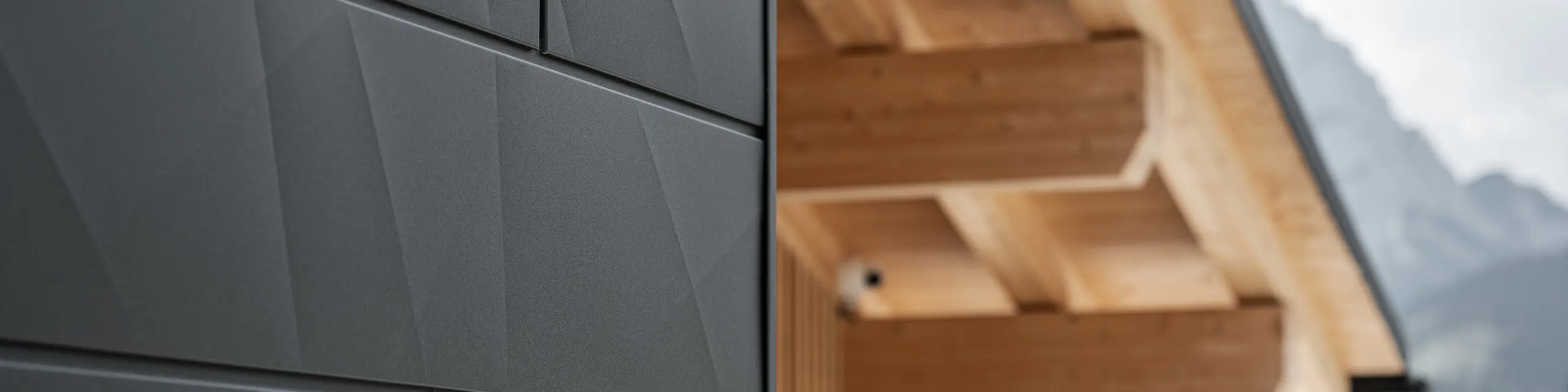 Närbild av Siding.X fasadpanelerna i P.10 svart från PREFA på Casa Hoffe i Sappada, Italien. Fasadsystemet i aluminium är omsorgsfullt monterat i en modern, abstrakt design som bildar en attraktiv kontrast till de synliga träelementen i takstolen. Den innovativa fasadlösningen smälter sömlöst in i den alpina atmosfären och illustrerar kombinationen av funktionalitet, hållbarhet och estetisk byggnadskultur.