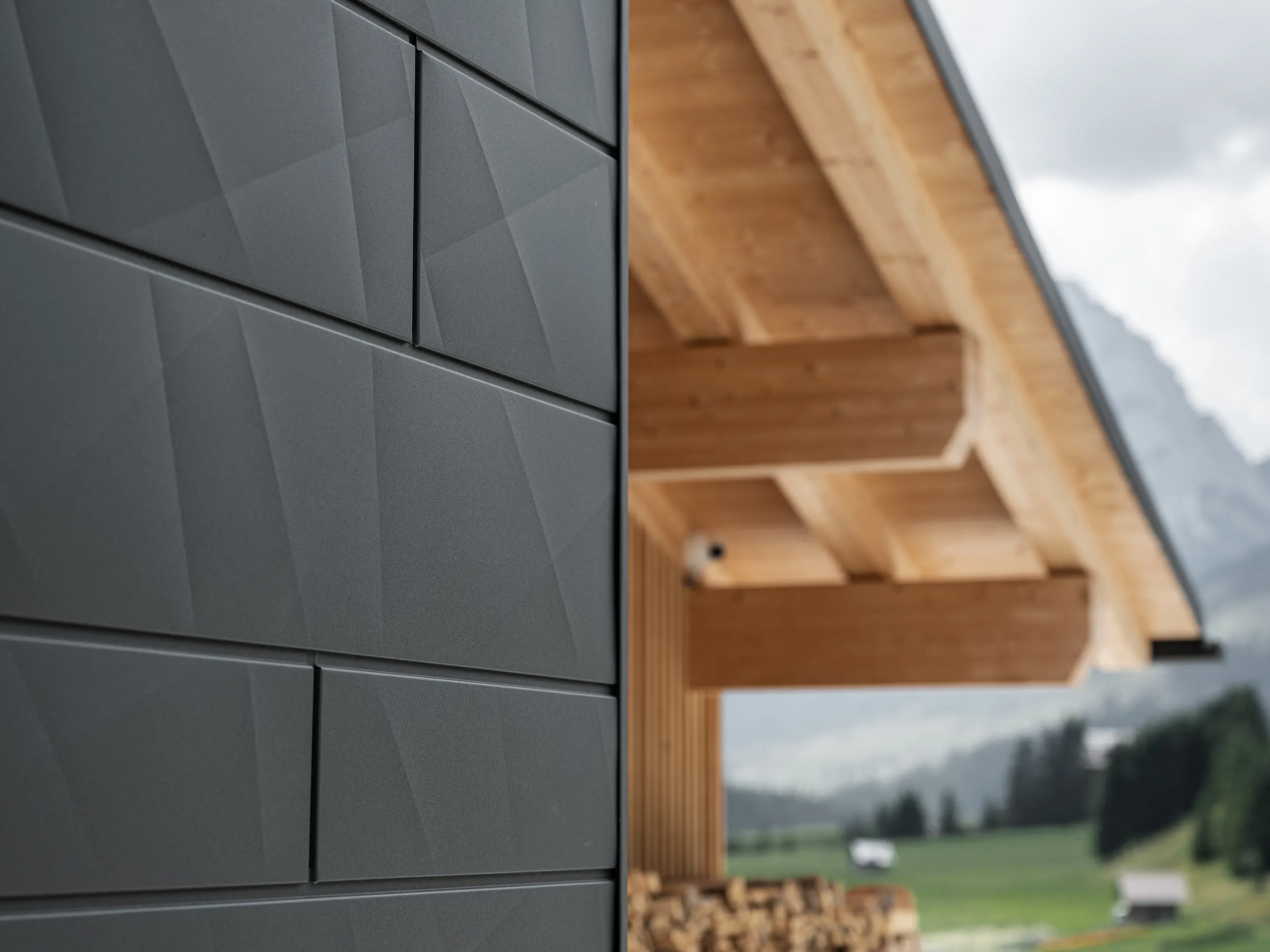 Närbild av Siding.X fasadpanelerna i P.10 svart från PREFA på Casa Hoffe i Sappada, Italien. Fasadsystemet i aluminium är omsorgsfullt monterat i en modern, abstrakt design som bildar en attraktiv kontrast till de synliga träelementen i takstolen. Den innovativa fasadlösningen smälter sömlöst in i den alpina atmosfären och illustrerar kombinationen av funktionalitet, hållbarhet och estetisk byggnadskultur.