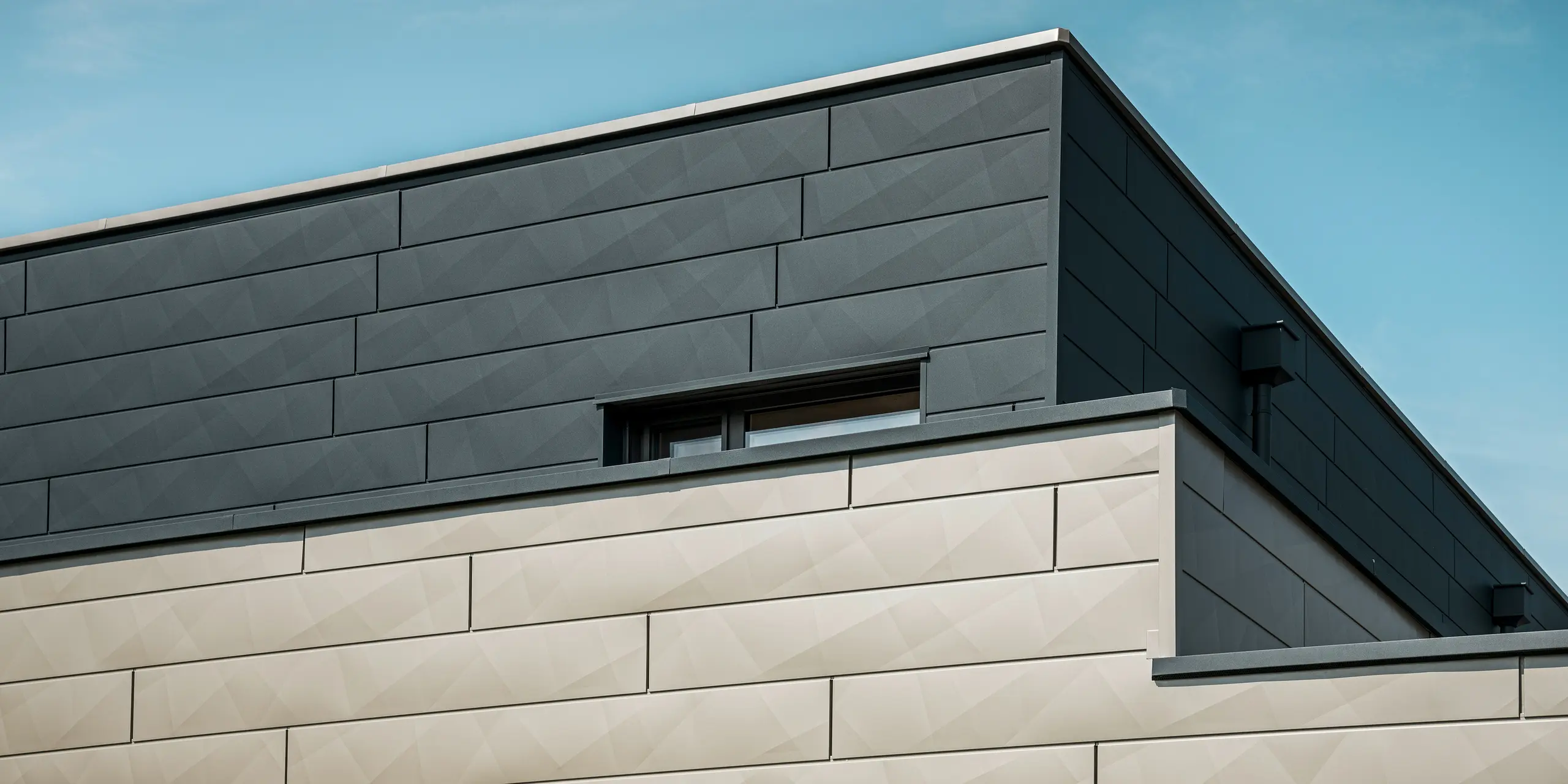 [Translate to Svenska:] Nahaufnahme der zweifarbigen PREFA Aluminiumfassade eines modernen Einfamilienhauses in Wippenham, Österreich. Die Fassade ist mit Siding.X Fassadenpaneelen in den Farben Anthrazit und Bronze gestaltet, die ein elegantes und dynamisches Erscheinungsbild erzeugen. Die präzise Verarbeitung und das Zusammenspiel der Farben betonen die zeitgemäße Architektur des Gebäudes.