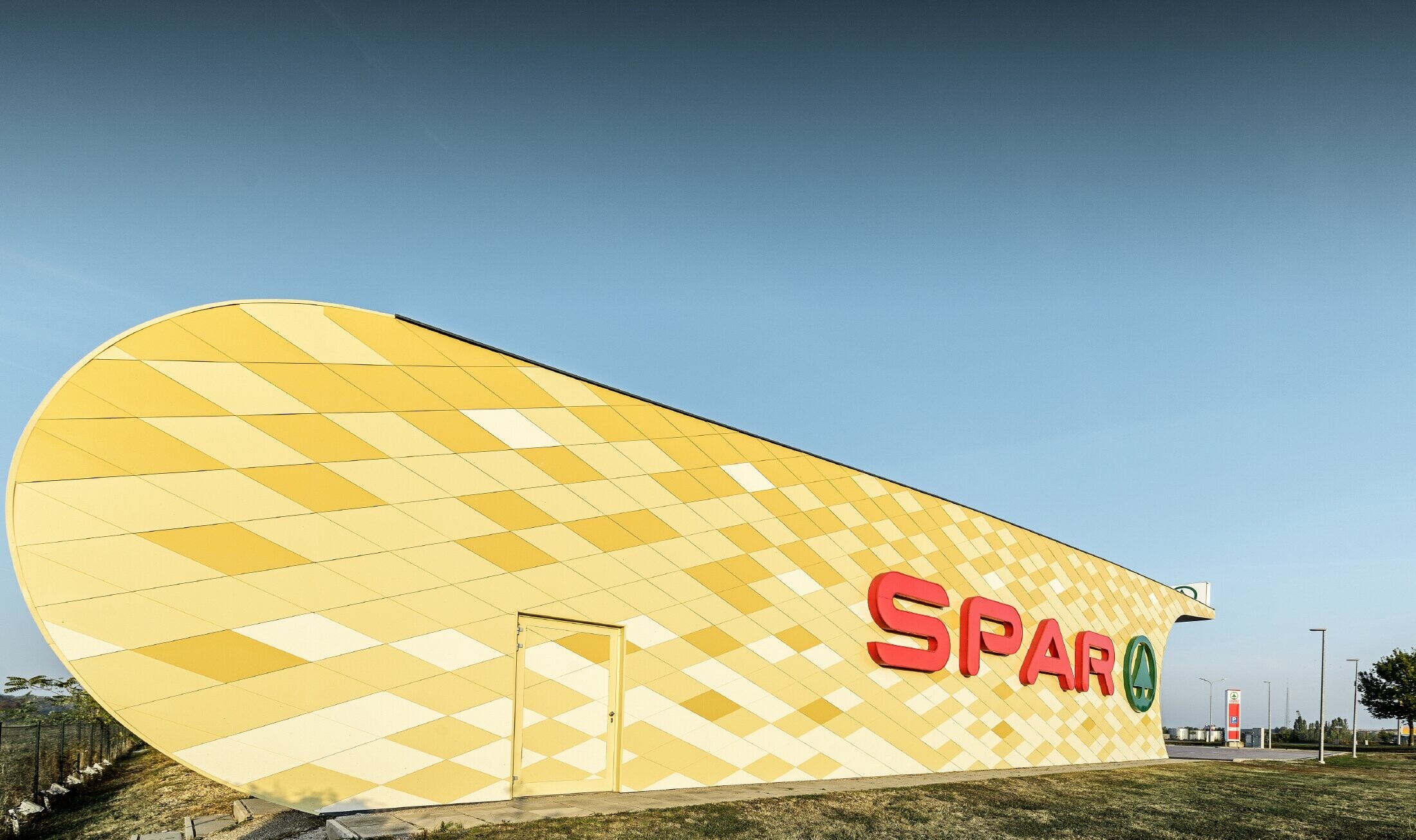 Spar-filial med en rutmönstrad aluminiumfasad i gulorange och Spar-logo