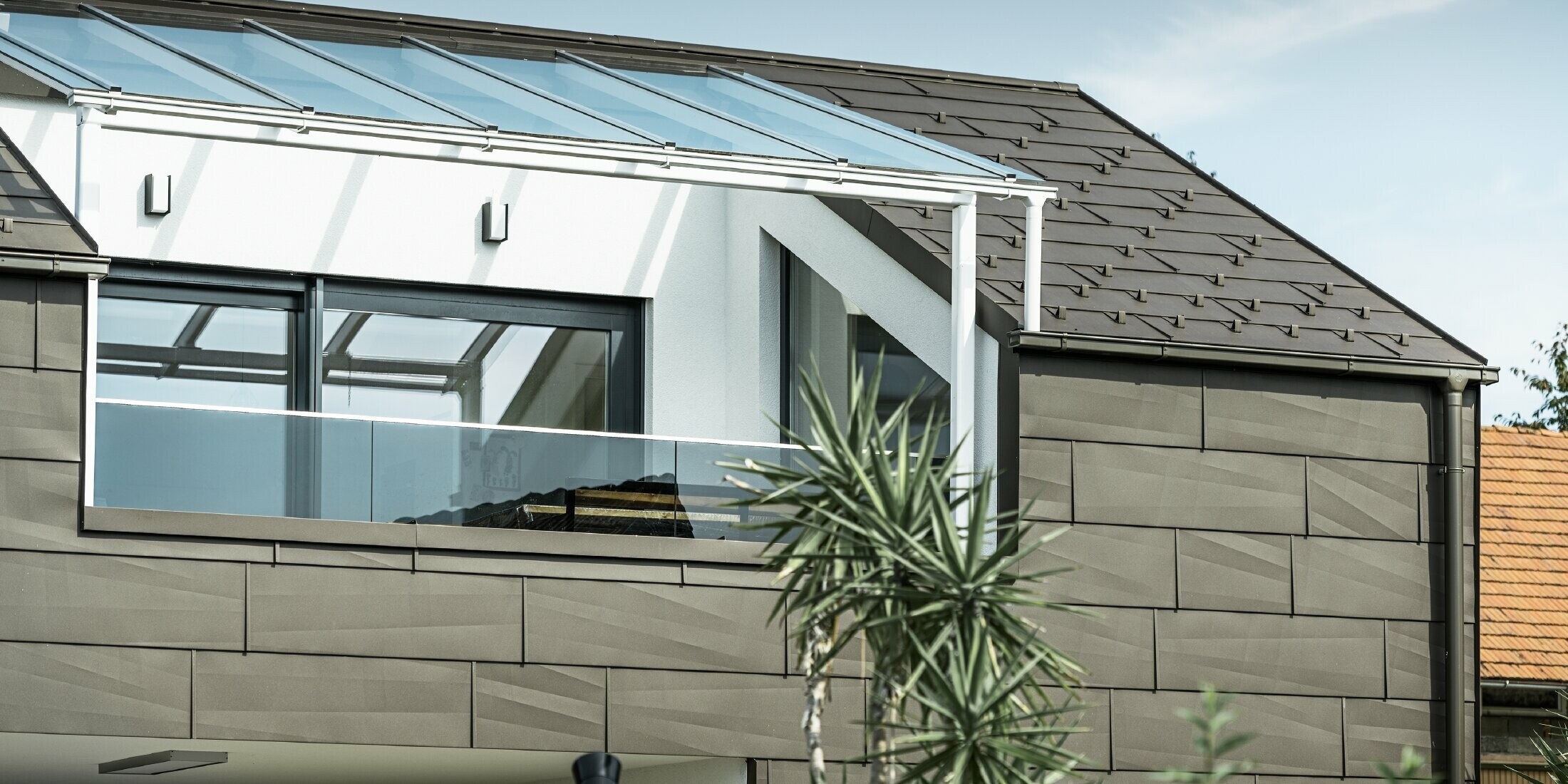 Tillbyggnad med takterrass täckt med PREFA komplett system. På tak och fasad användes PREFA tak- och fasadpanel FX.12. Dessutom används PREFA rektangulär ränna, PREFA stuprör och omfattande tillbehör i brunt för takavvattningen.