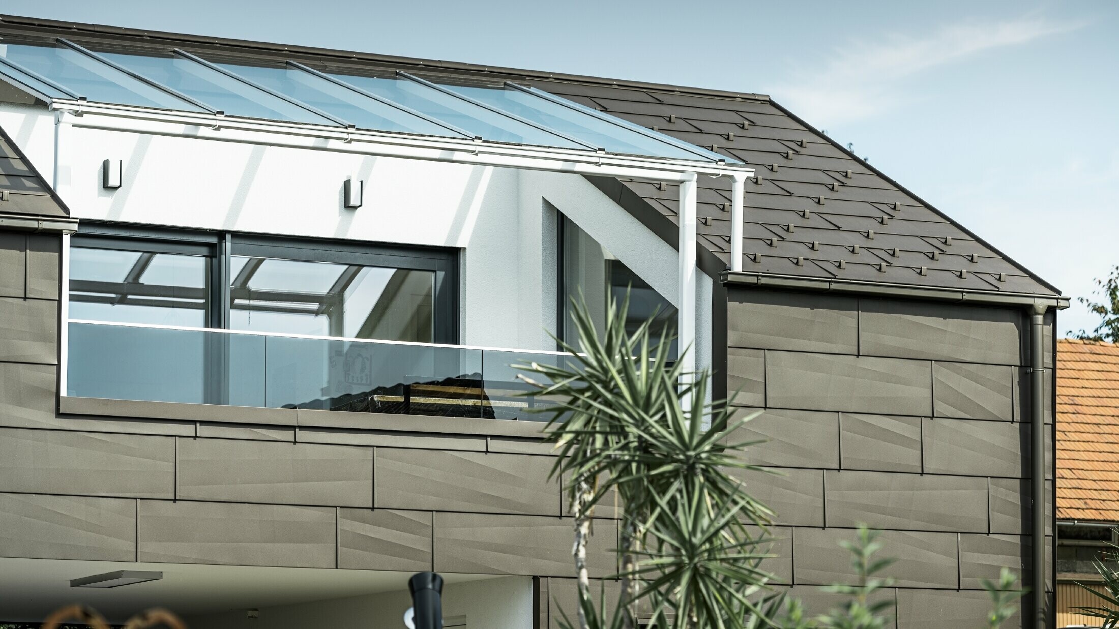 Tillbyggnad med takterrass täckt med PREFA komplett system. På tak och fasad användes PREFA tak- och fasadpanel FX.12. Dessutom används PREFA rektangulär ränna, PREFA stuprör och omfattande tillbehör i brunt för takavvattningen.