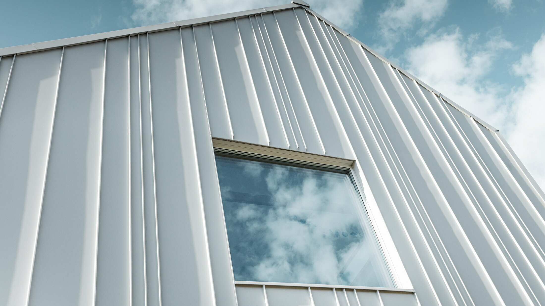 vit PREFALZ som vinklad stående vinkelfals på fasaden med olika panelbredder och ett fönster