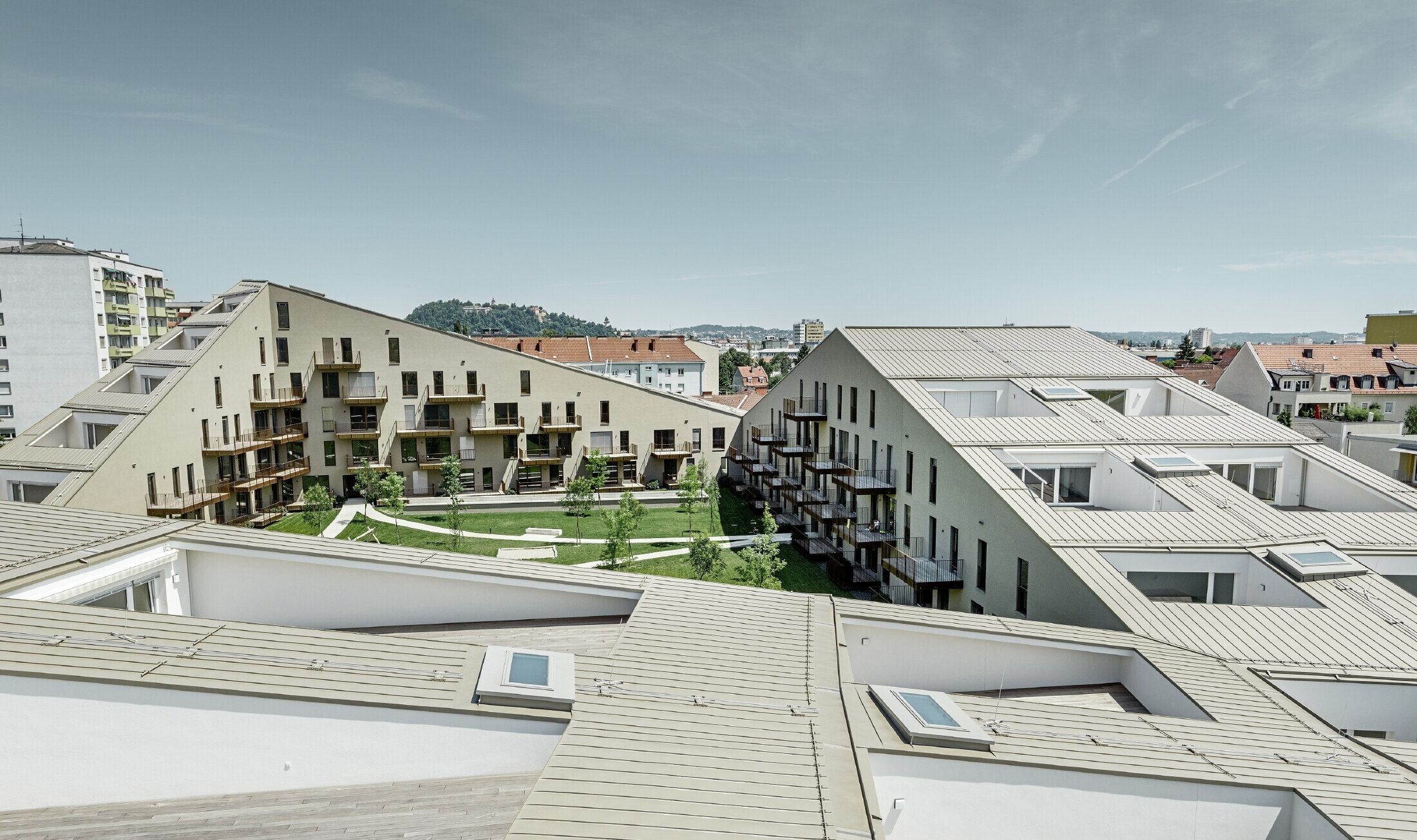 långsträckt bostadsbyggnad i Graz med plana takytor och integrerade terrasser och generösa fönster med ett prefalztak i specialfärgen bronsmetallic
