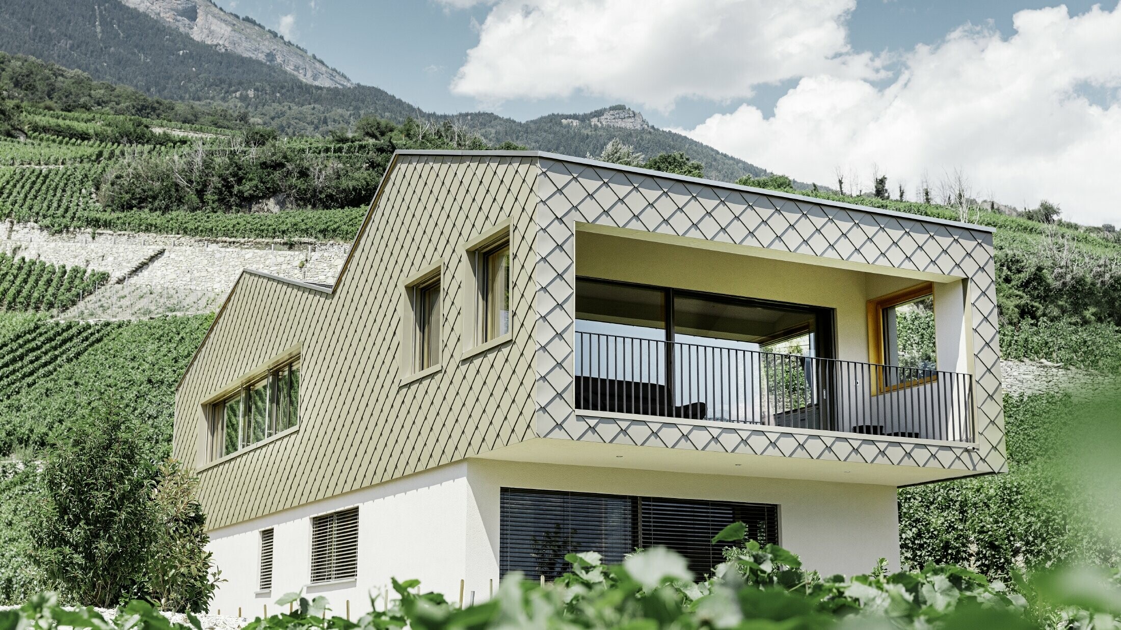 modernt enfamiljshus mitt bland vinbergen i Rhônedalen med 4 olika takytor och ett öppet galleri med en rombfasad i brons