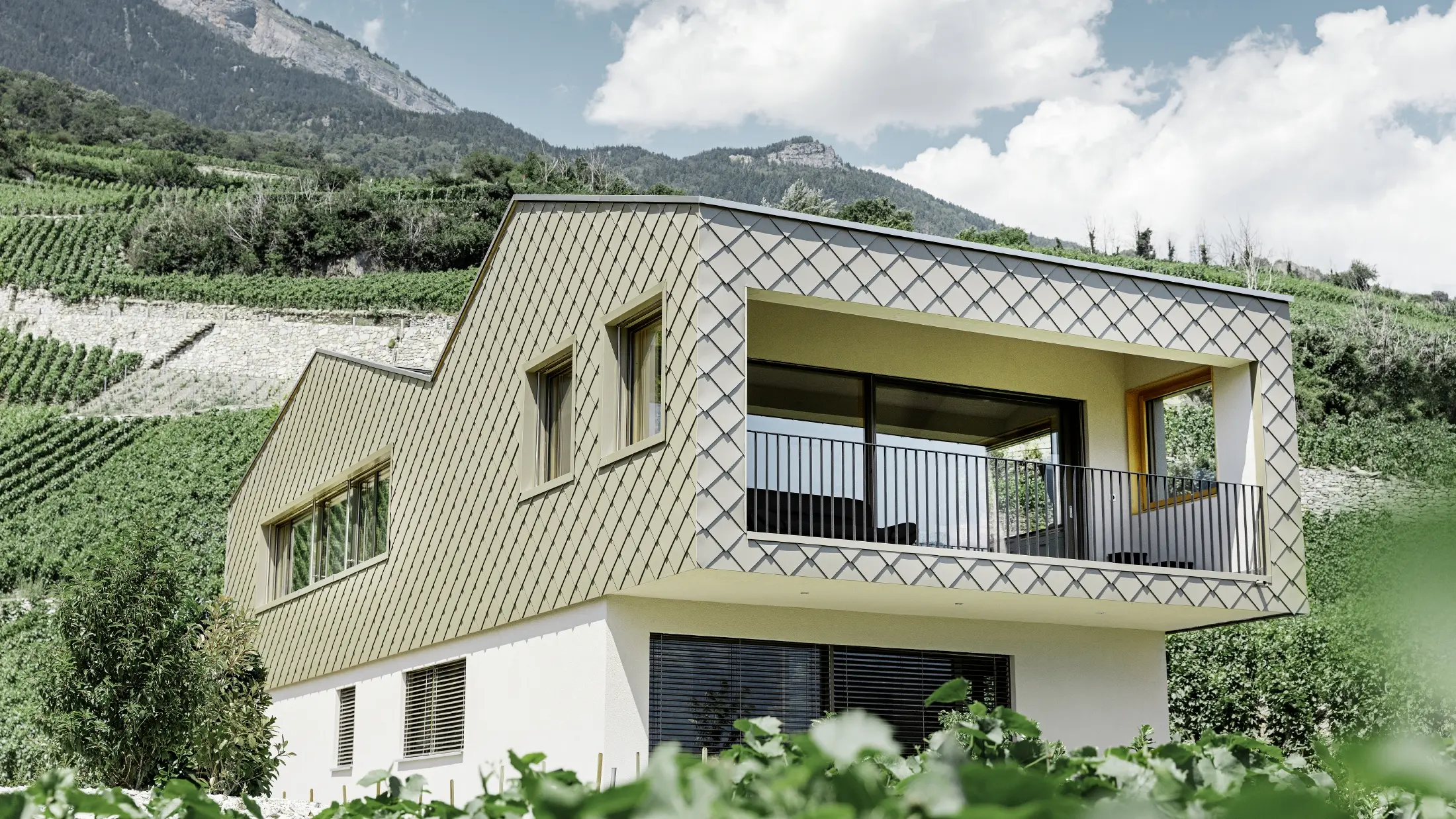 modernt enfamiljshus mitt bland vinbergen i Rhônedalen med 4 olika takytor och ett öppet galleri med en rombfasad i brons
