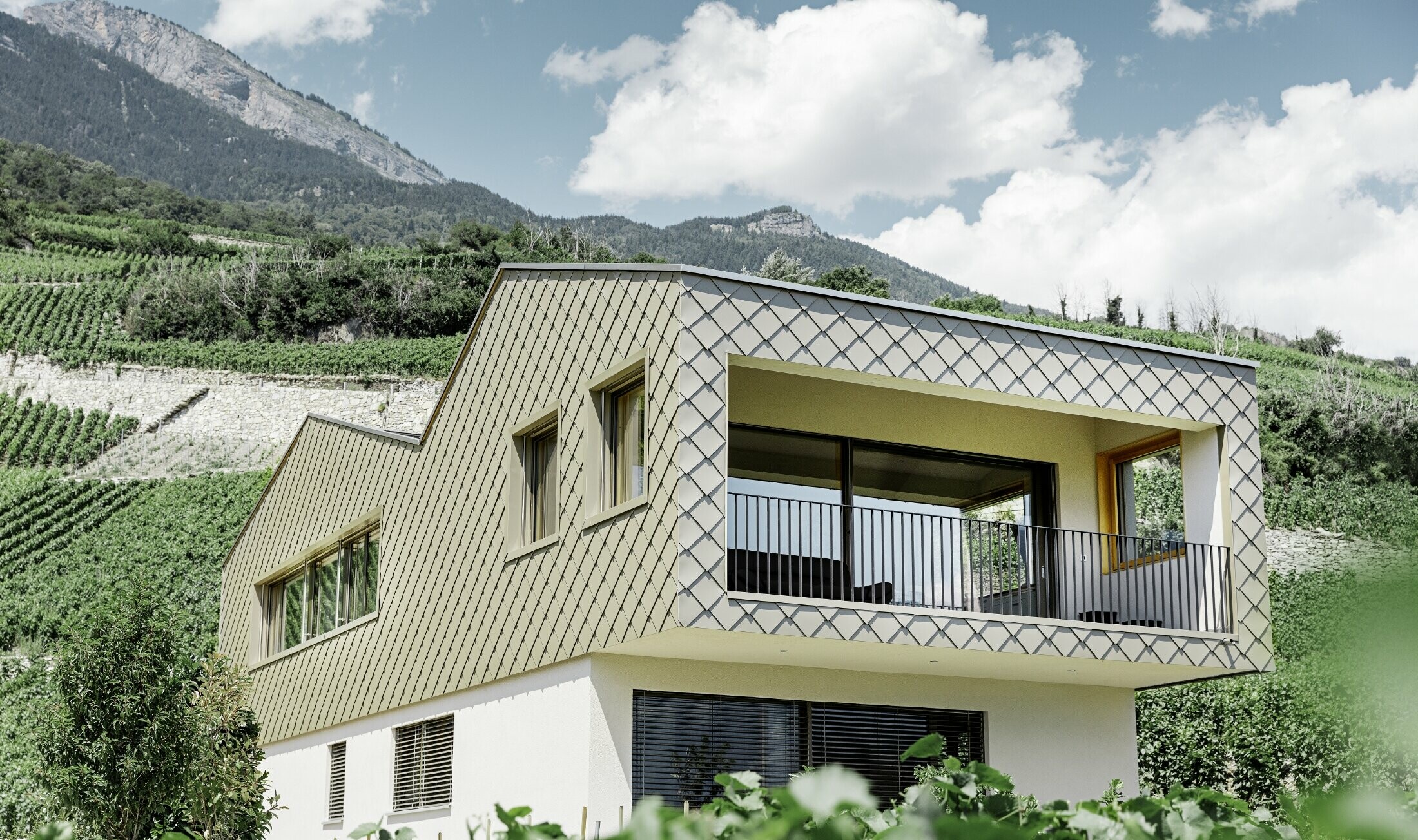 modernt enfamiljshus mitt bland vinbergen i Rhônedalen med 4 olika takytor och ett öppet galleri med en rombfasad i brons