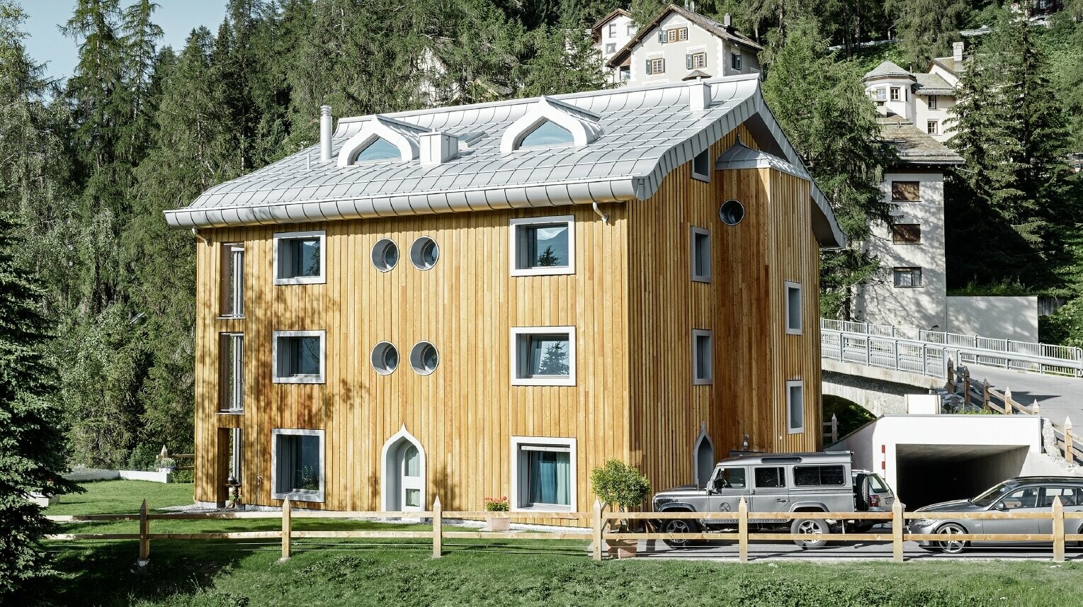 Bostadsbyggnad i St. Moritz med träfasad och aluminiumtak med svängda takskenor i silvermetallic