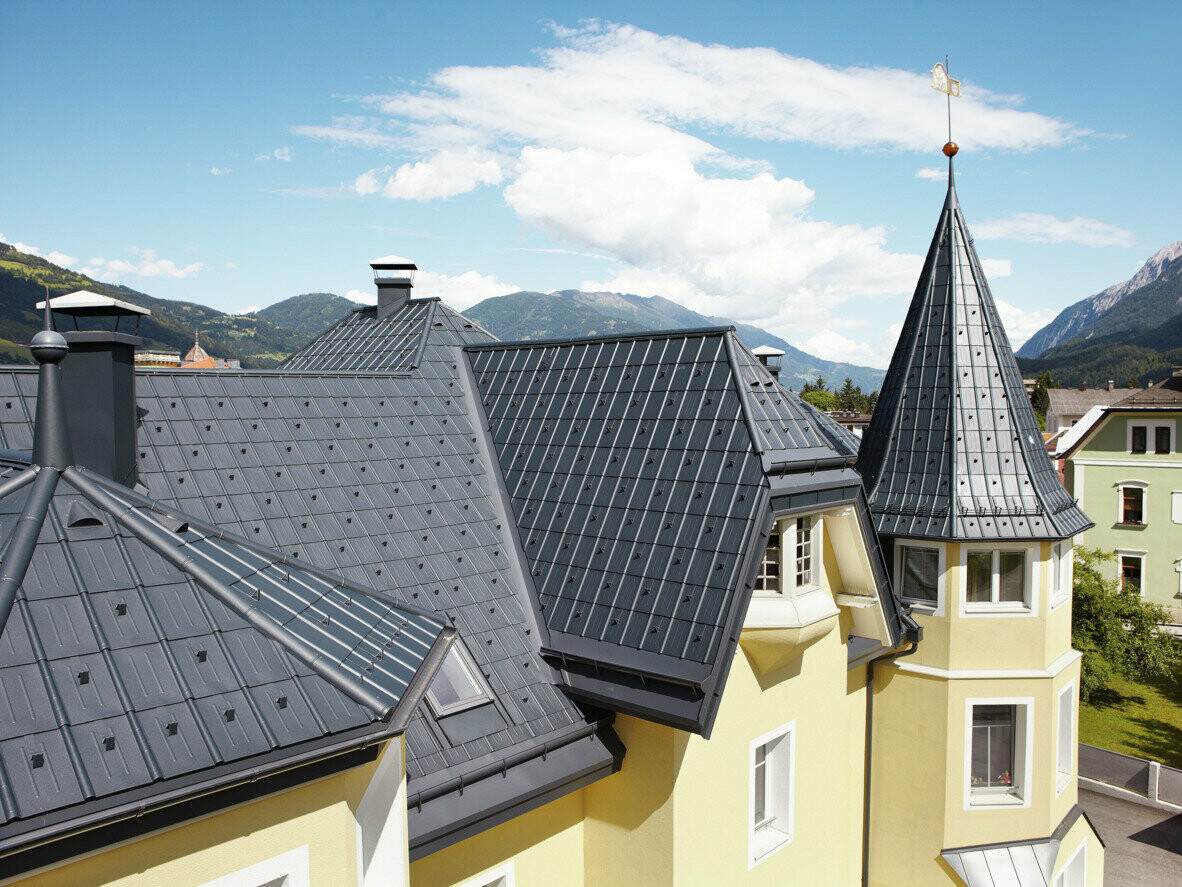 Byggnad med många detaljer, torn och vinklade takytor; Taket är täckt med PREFA takplatta i antracit. För takavvattningen används PREFA hängränna samt PREFA fotränna i antracit.