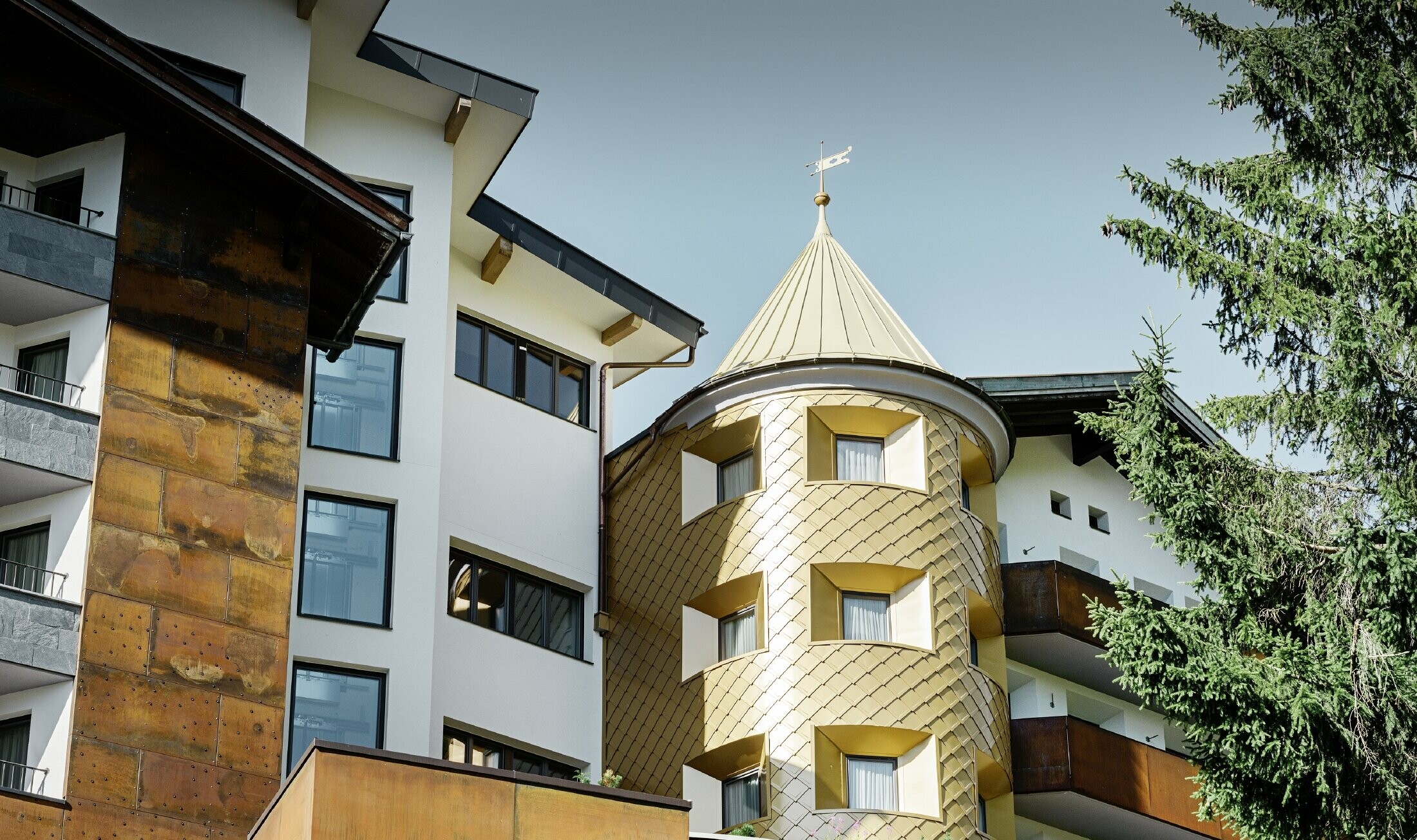 traditionellt hotell i Ischgl med träbalkonger och träfasad och ett torn med guldfärgade aluminiumromber från PREFA
