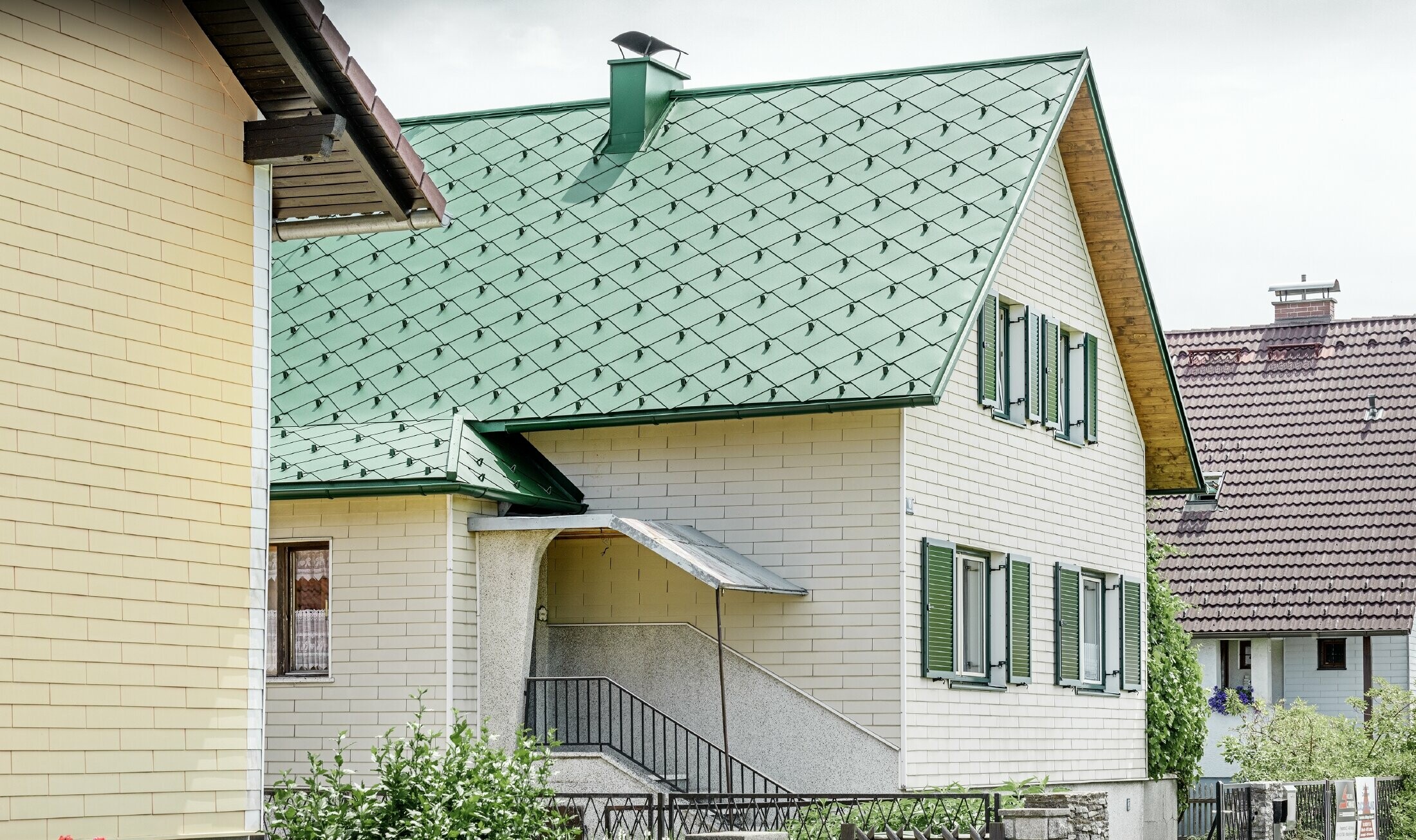 Klassiskt enfamiljshus med ett mossgrönt sadeltak i aluminium och gröna fönsterluckor