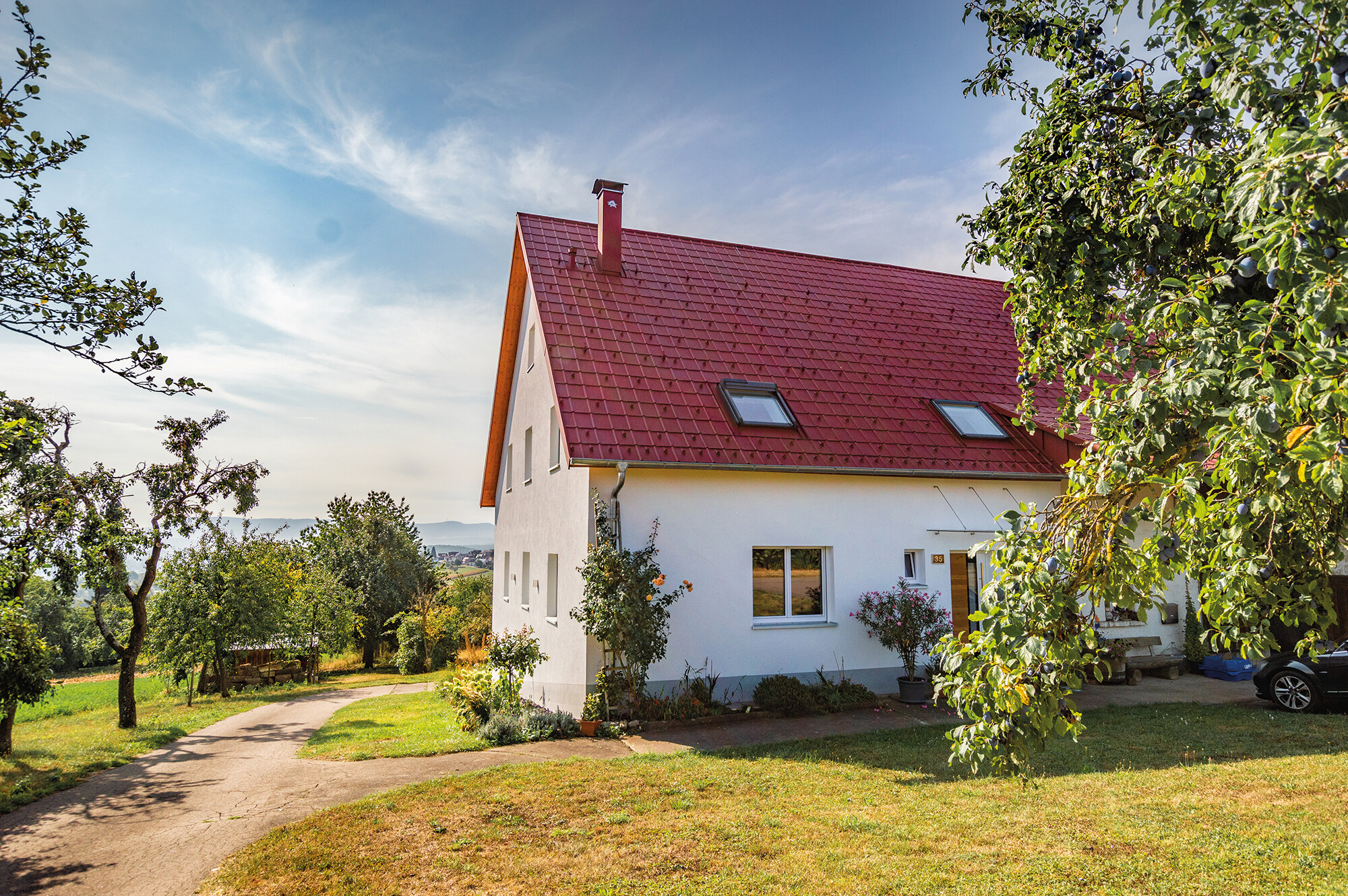 Romantiskt litet hus på landsbygden med massor av träd och buskar. Täckt med ett tak från PREFA i oxidrött.