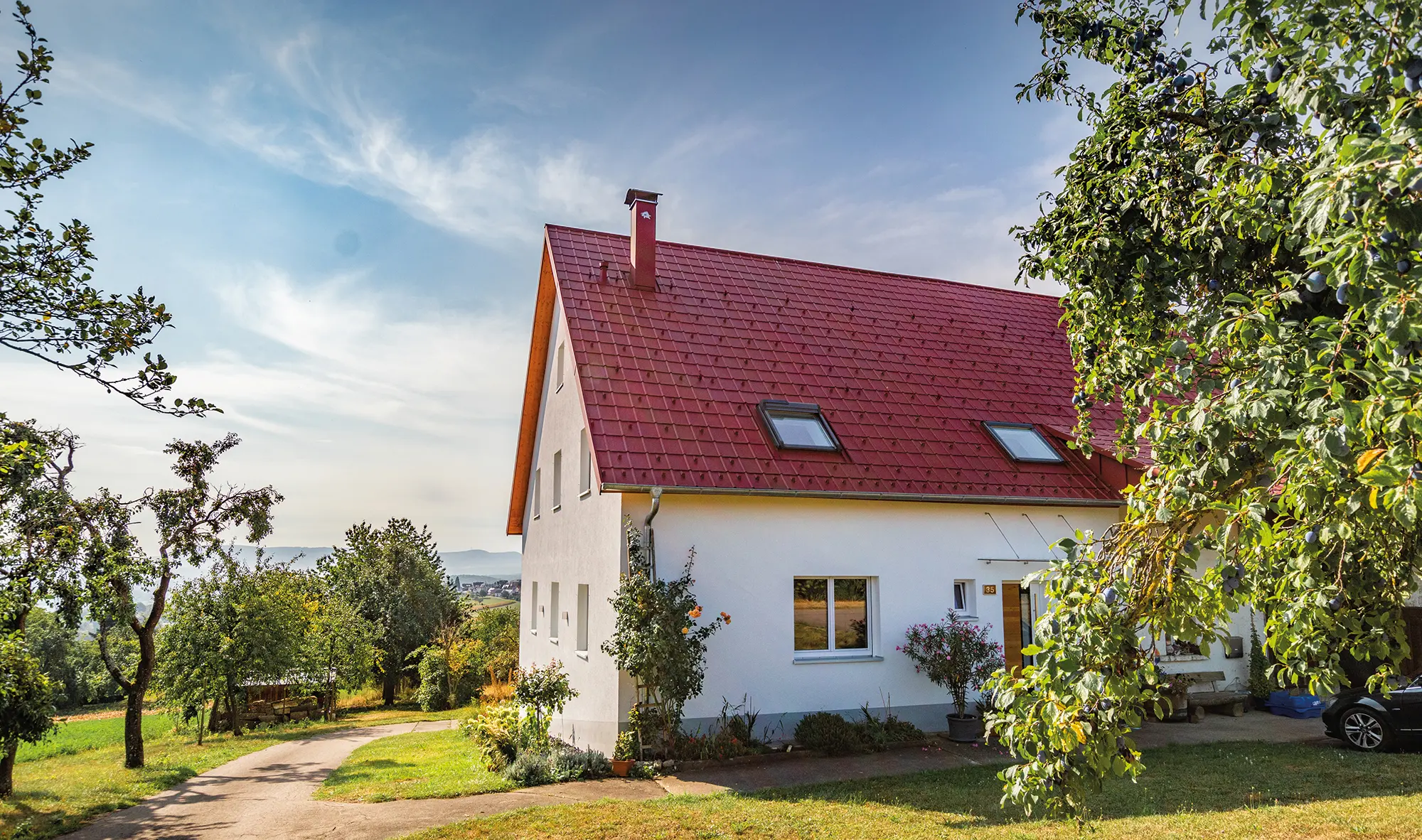 Romantiskt litet hus på landsbygden med massor av träd och buskar. Täckt med ett tak från PREFA i oxidrött.