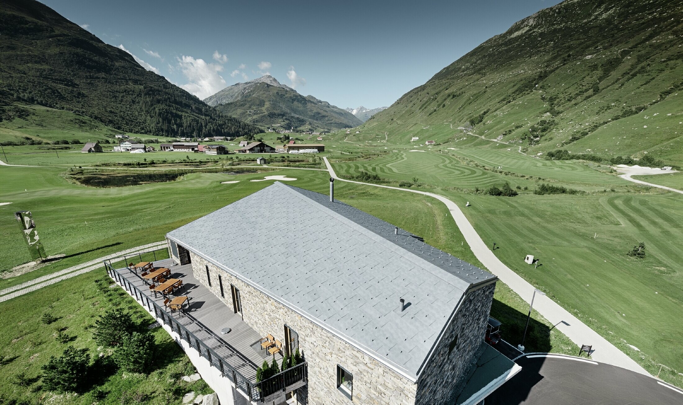 Modernt klubbhus vid golfbanan i Andermatt med stenfasad och PREFA:s takpanel FX.12 av aluminium i stengrått