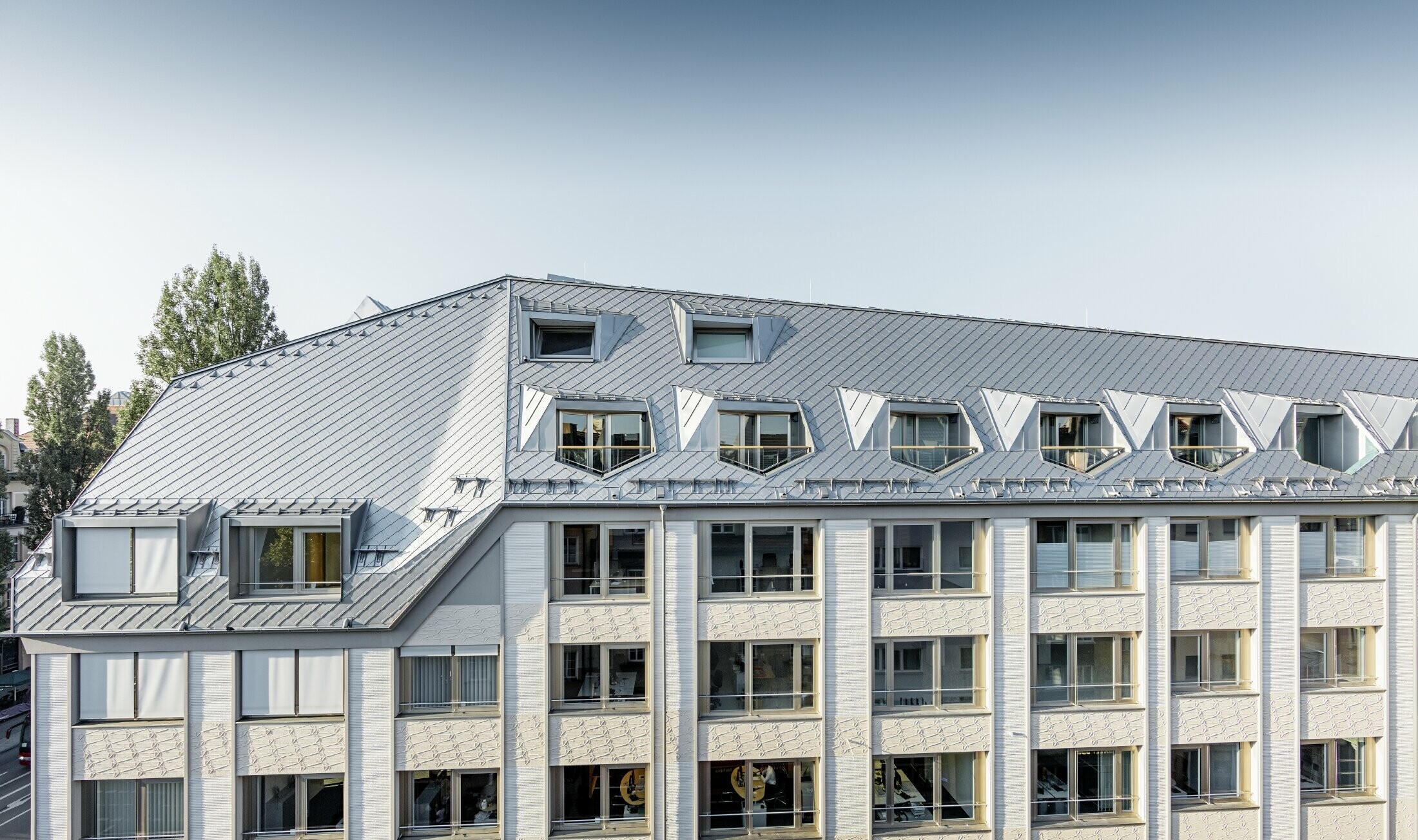 Renoverade mansardvåningar med de generösa, öppna gallerinivåerna hos ett bostads- och affärshus på Leopoldstraße i München, med en takläggning av takromber från PREFA