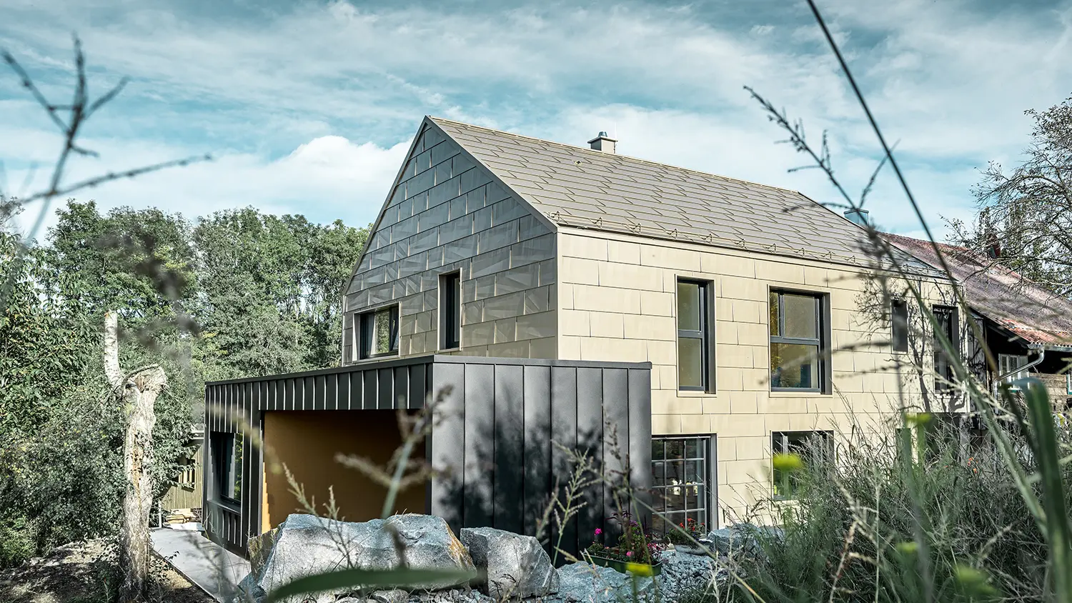 Tak och fasad på bostadshus utan taksprång är täckt med aluminiumpanel FX.12 från PREFA i brons. Precis bredvid står ett garage med flackt tak med en fasad med stående vinkelfals.