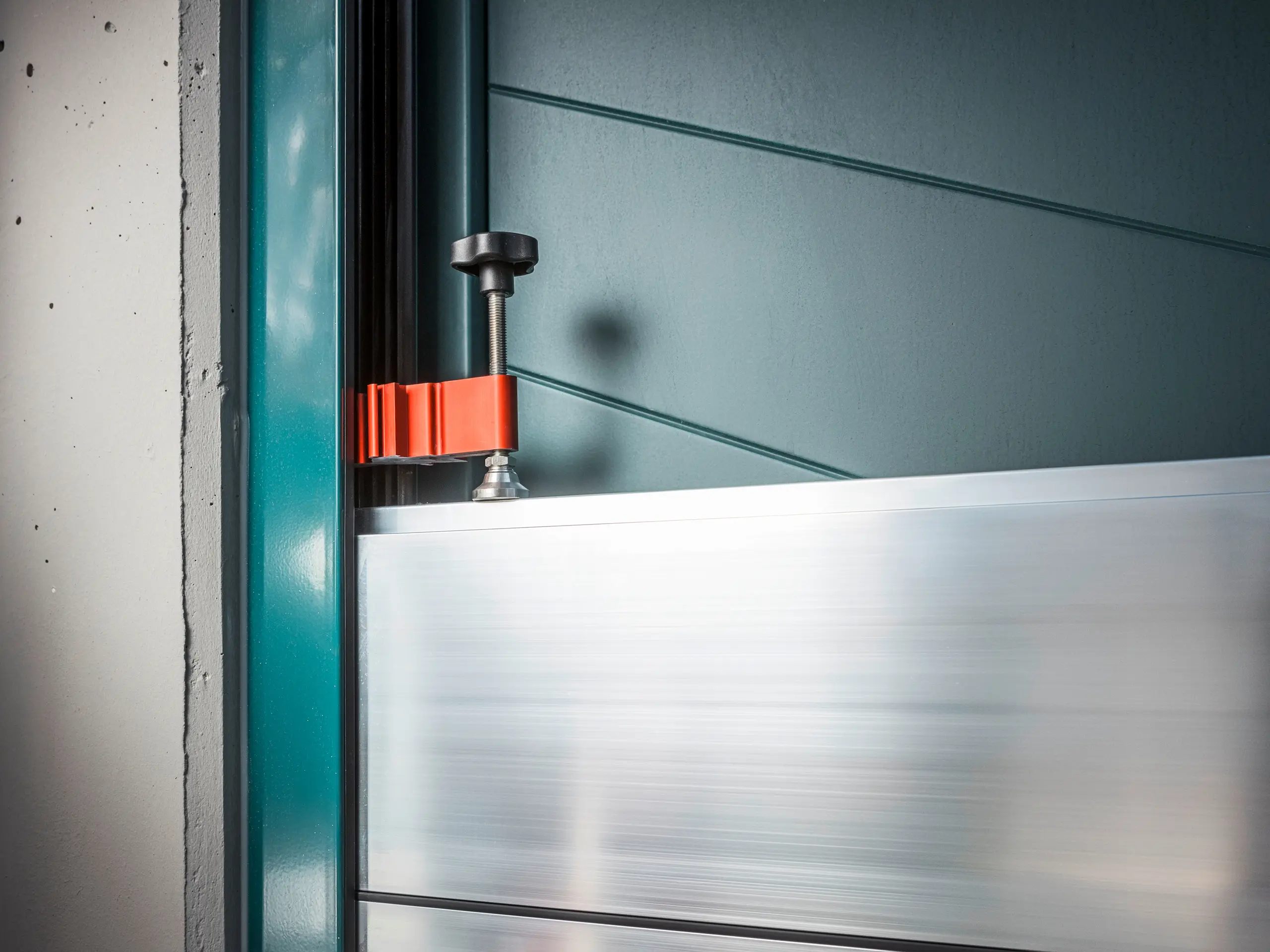 Närbild av översvämningsskyddet PREFA på en grindram, bestående av aluminiumbalkar som fästs med en robust, röd klämma (klämstycket) för att garantera ett säkert skydd mot översvämningar.
