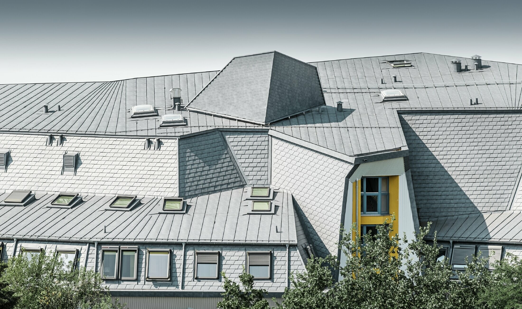 Inkapslat taklandskap med takkupoler och talrika vinklar på huset Aja Textor-Goethe, täckt med PREFA takshingel och Prefalz i stengrått