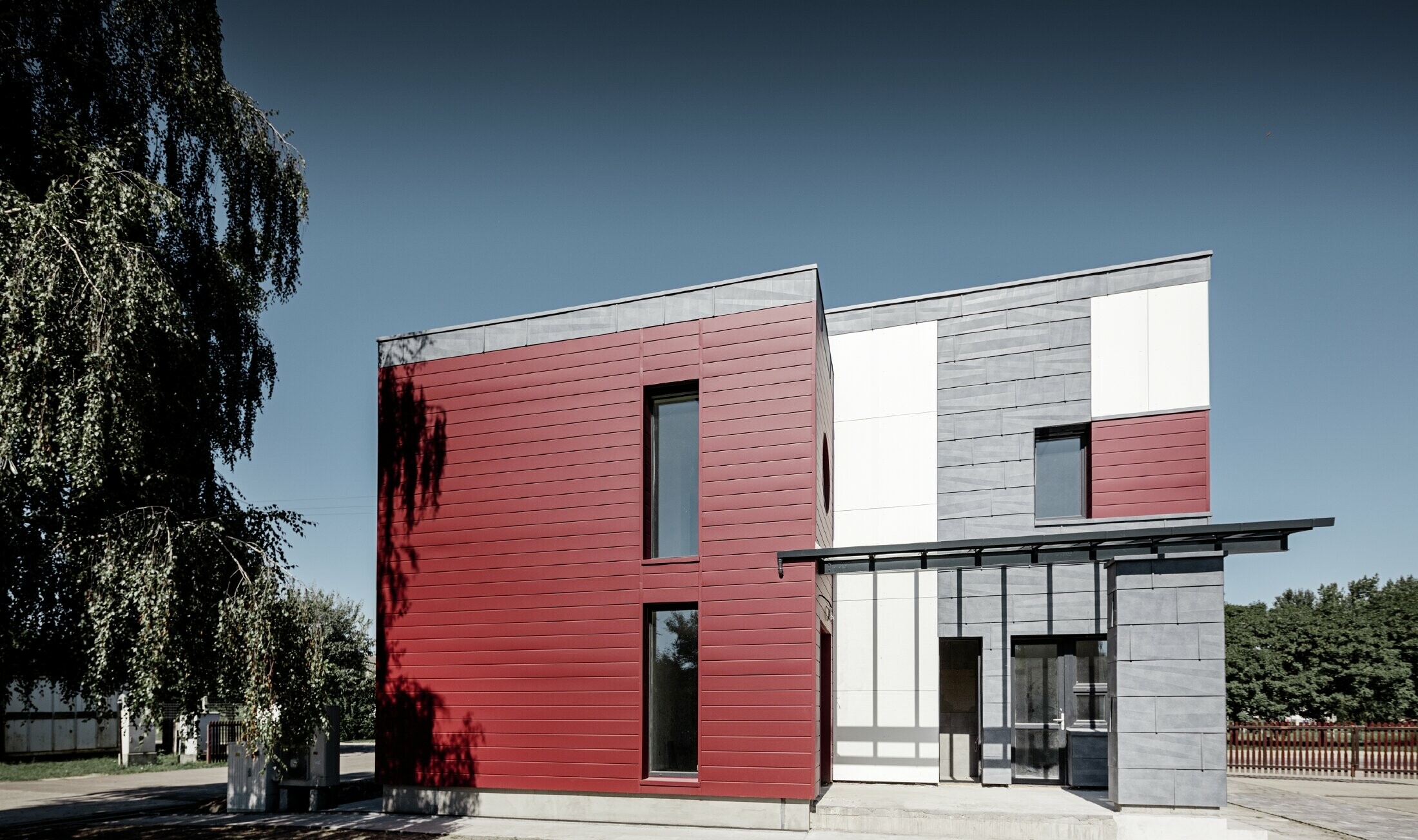 Modern kontorsbyggnad med en delad fasad i rött, stengrått och vitt med aluminiumprodukterna fasadpanel, fasadpanel FX.12 och samverkansplatta i aluminium från PREFA