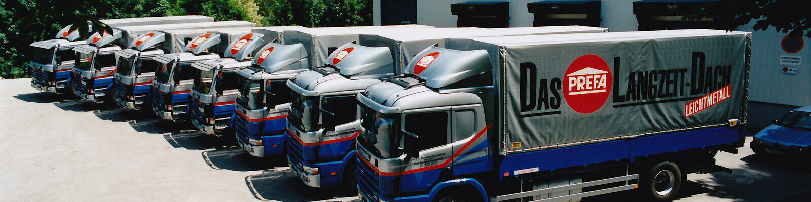 Åtta tidigare PREFA-lastbilar i blått och silver med PREFAs logotyp står på rad 