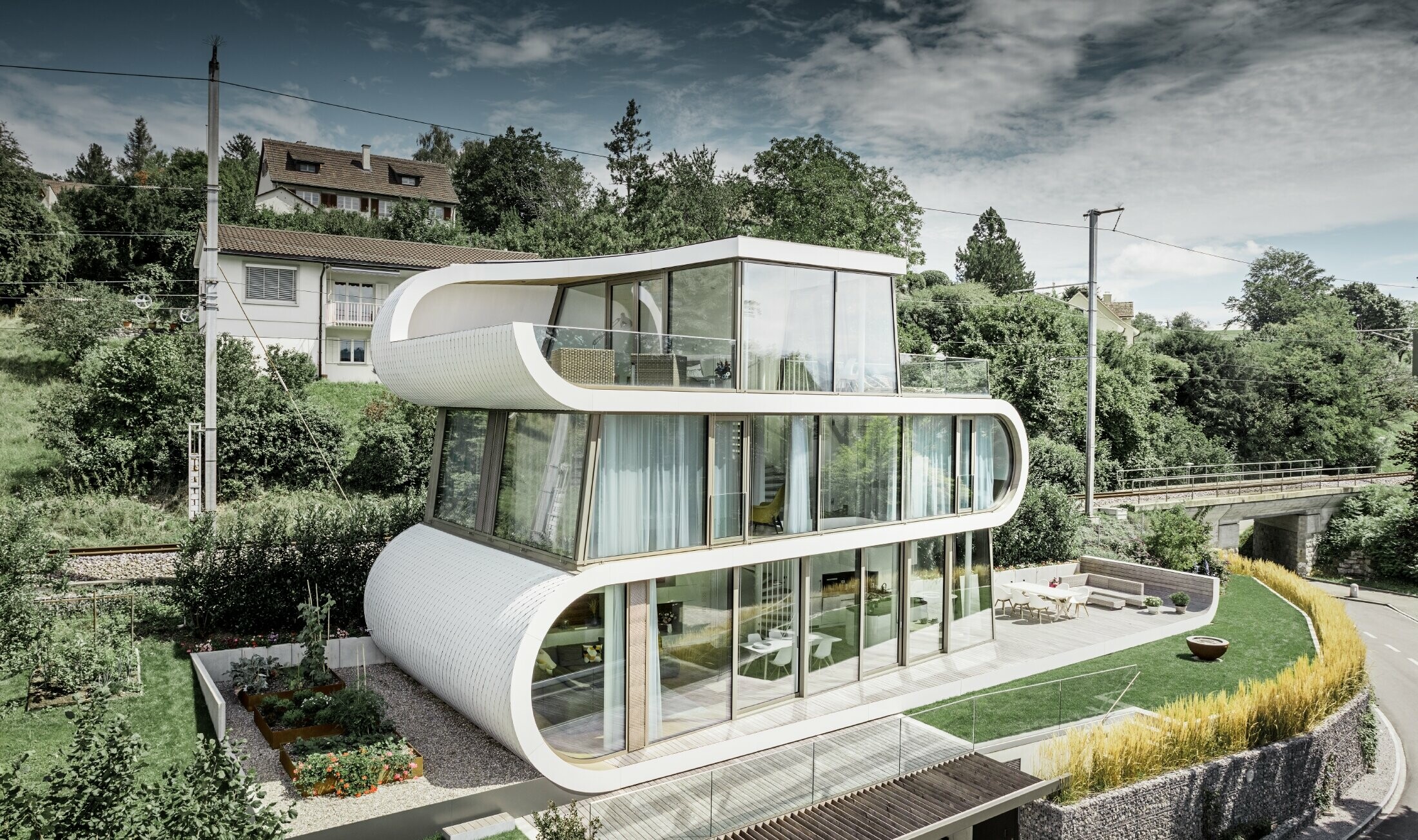 Mycket modernt familjhem designat av arkitekten Camenzind från Zürich. Ett böljande band förbinder de individuella våningarna. Kurvorna kläddes i renvitt med små takplattor från PREFA. Huset har många och stora glaspartier, vilket får hela huset att verka mycket öppet. 