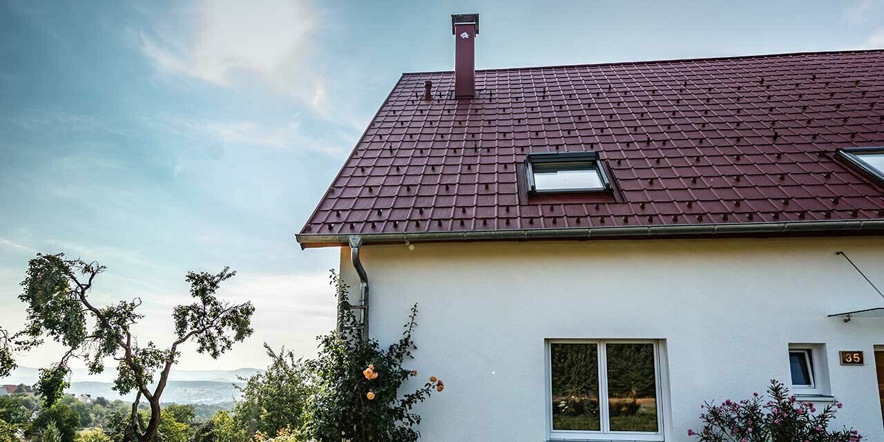 Litet hus på landet, nyrenoverat tak med PREFA takplattor i oxidrött, takfönster och skorstensinfattning.