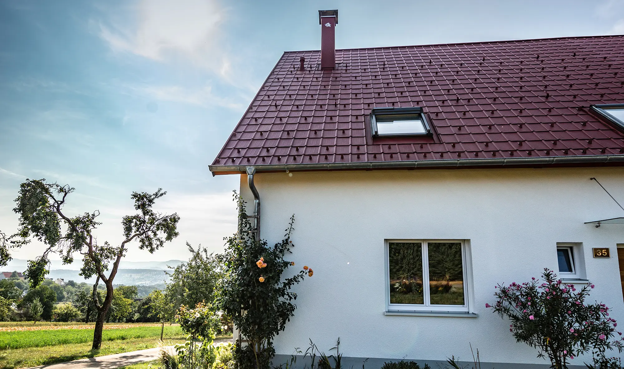 Litet hus på landet, nyrenoverat tak med PREFA takplattor i oxidrött, takfönster och skorstensinfattning.