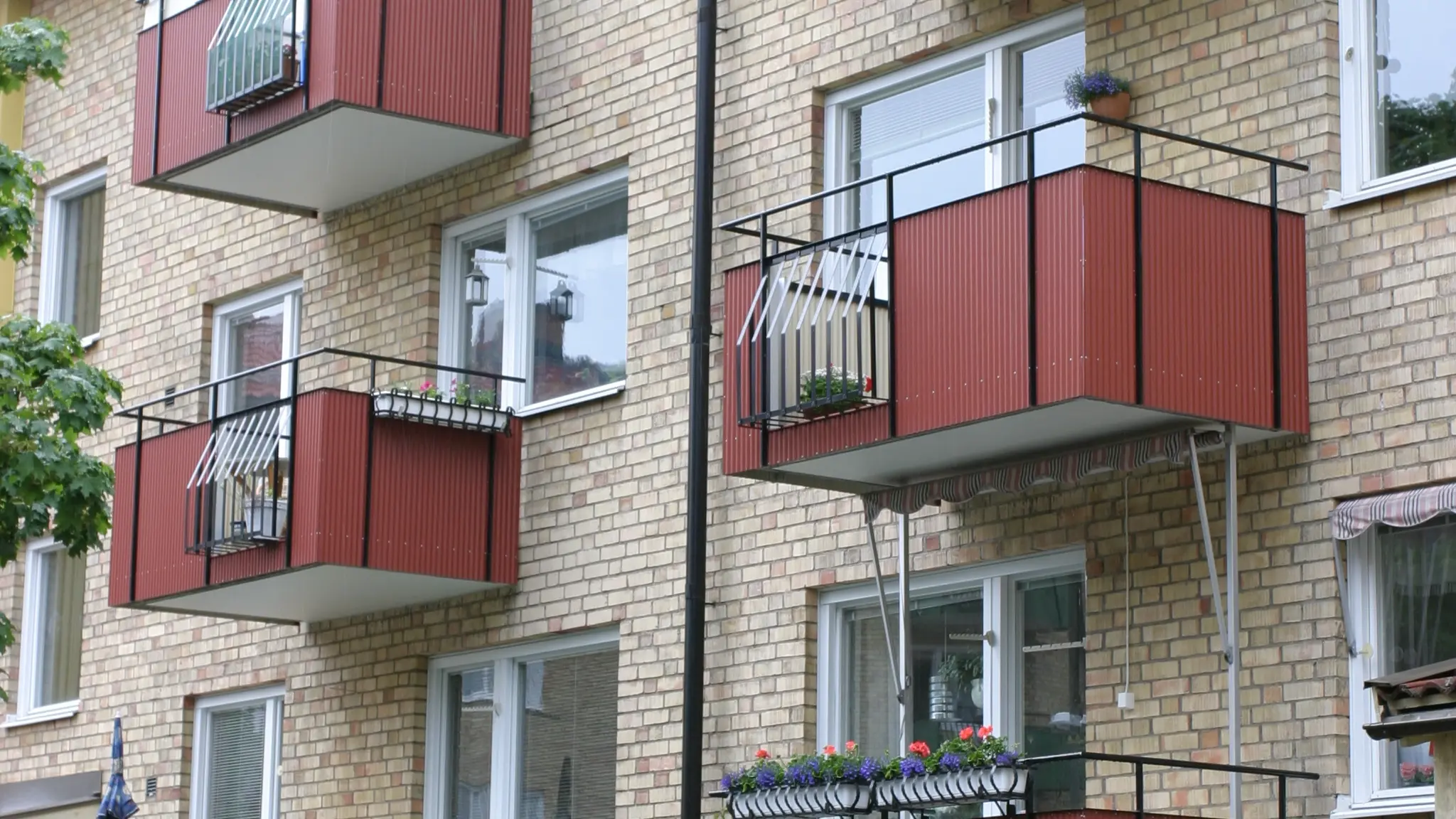 Klassiska balkonger på ett flerfamiljshus, klädda med gnejsröd Alustucco som kontrasterar mot tegelfasaden och får balkongerna att sticka ut.