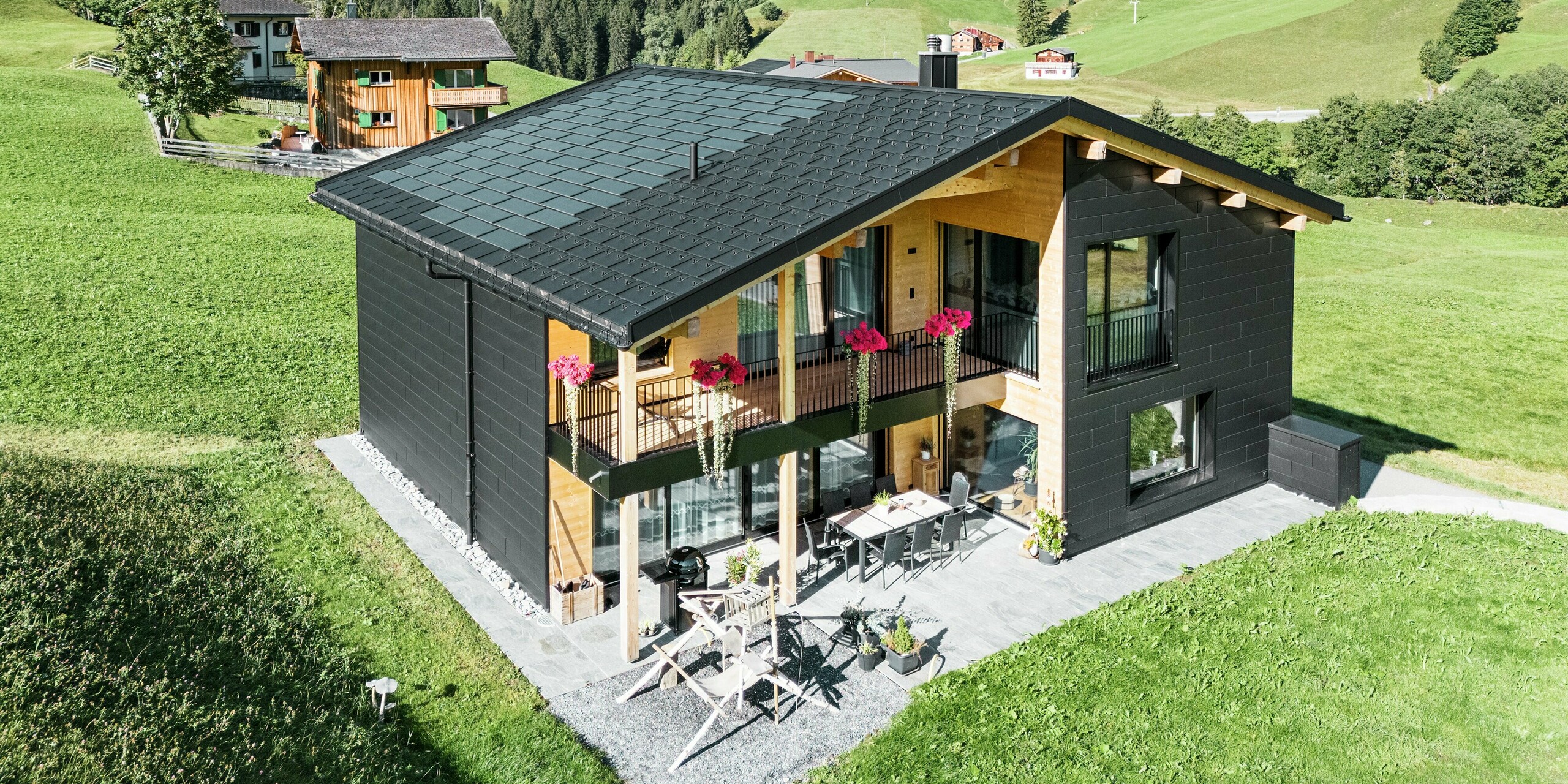 Det eleganta egnahemshuset i den kuperade omgivningen i Ascharina (Schweiz) visar hur aluminium och trä kan kombineras på ett perfekt sätt. De robusta PREFA Siding.X-fasadpanelerna i svart P.10 harmonierar med taket som består av PREFA solcellstakpaneler och R.16-takpaneler i samma färgbeläggning. Den hållbara aluminiumbeklädnaden skyddar byggnaden på ett tillförlitligt sätt mot utmaningarna i det alpina klimatet.