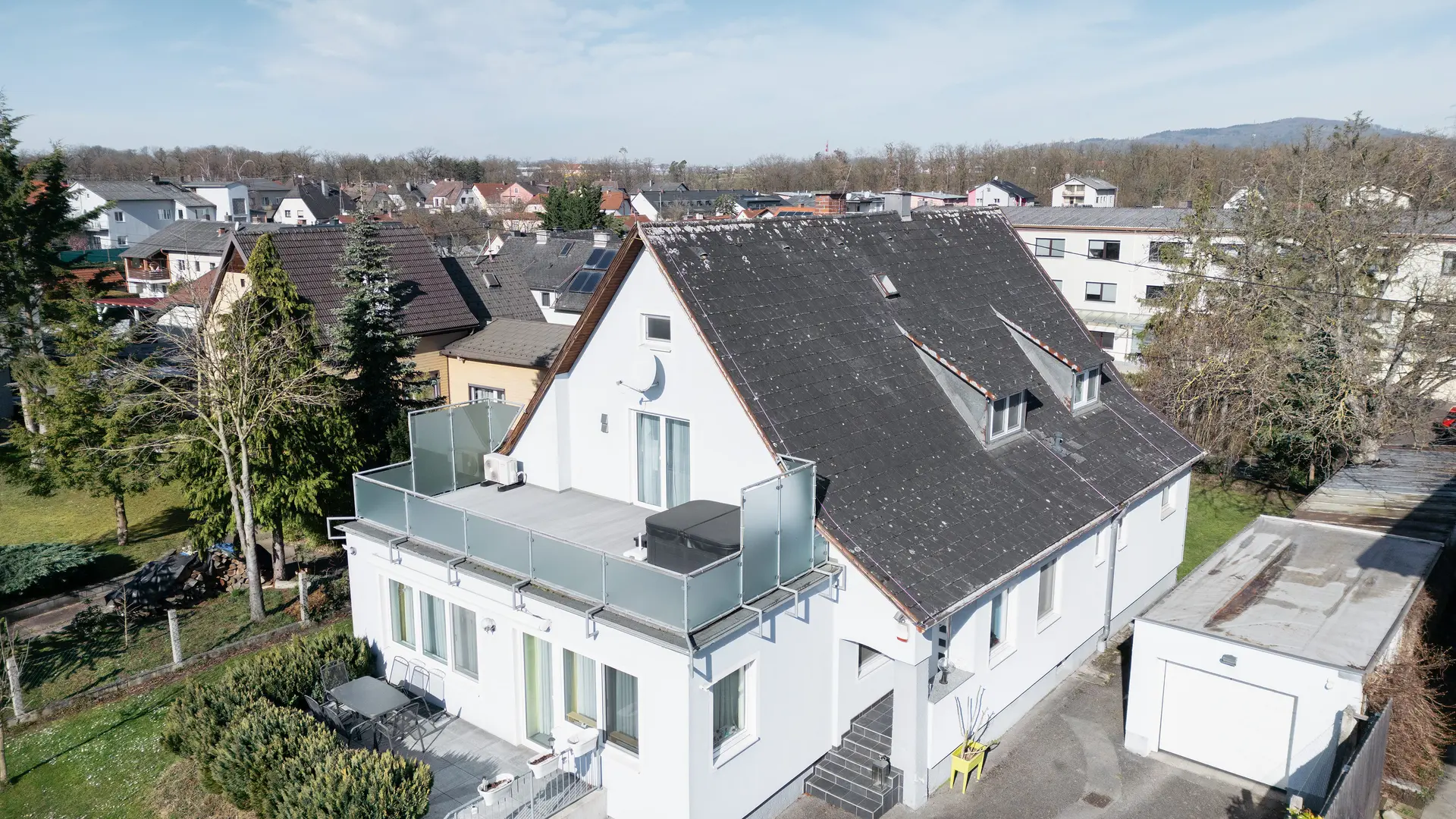 Fågelperspektiv på en byggnad med ett gammalt eternit-tak som är täckt av smuts och lav. Inga solcellsanläggningar syns på taket. Balkongen i förgrunden har glasräcke och ligger på byggnadens översta våning.