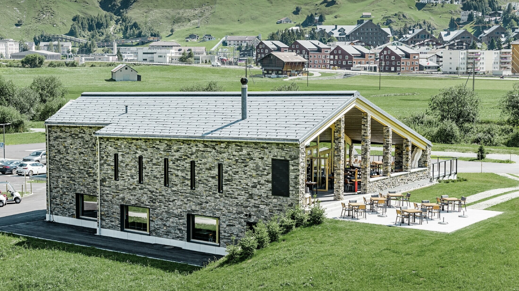 Modernt klubbhus vid golfbanan i Andermatt med stenfasad och PREFA:s takpanel FX.12 av aluminium i stengrått