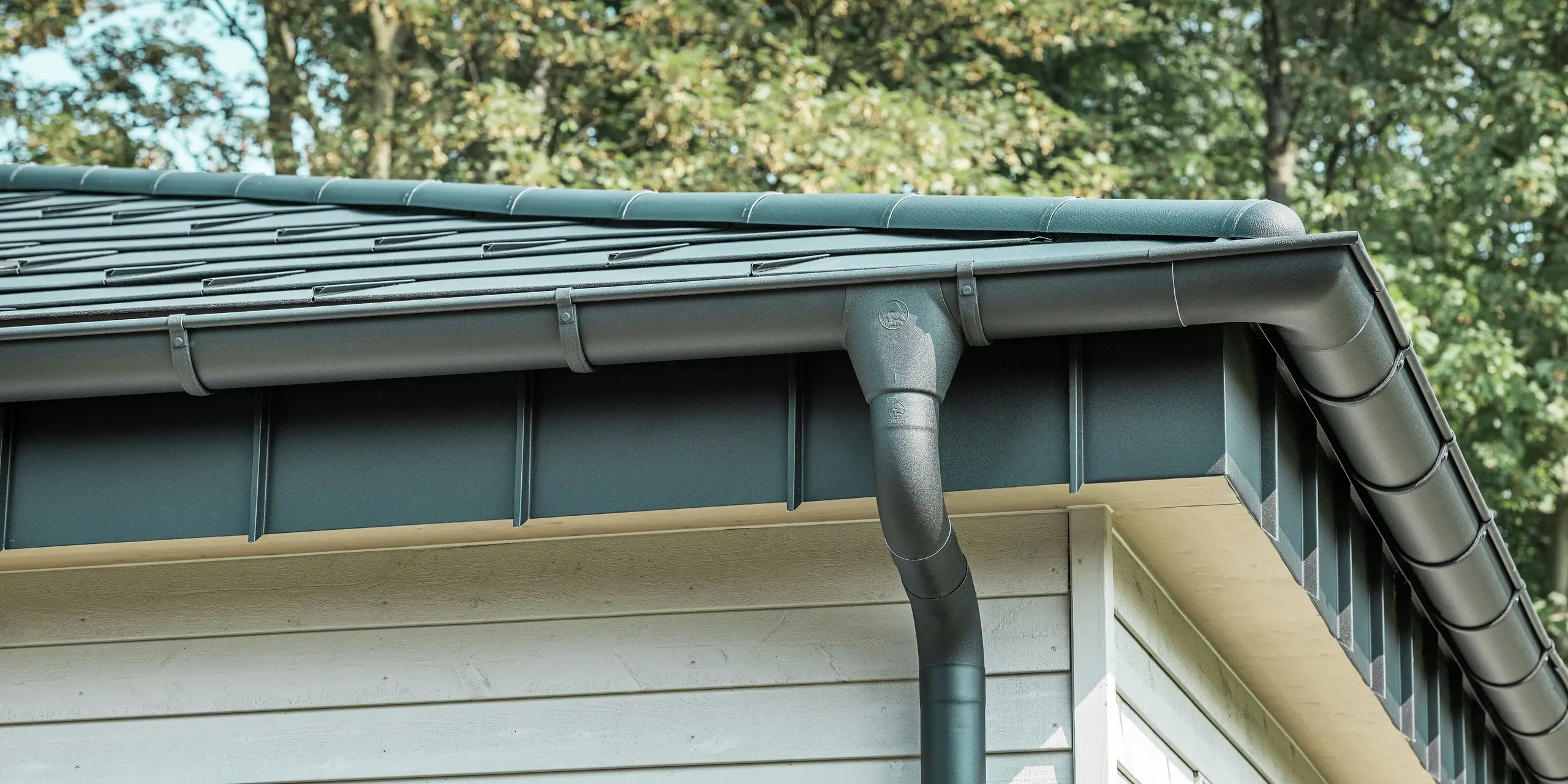 Detaljbild av PREFA Takavvattning på en bungalow i Rommerskirchen. Den högkvalitativa takrännan och avloppsröret i P.10 Svart ger en säker takavvattning vid regn. De hållbara PREFA aluminiumprodukterna kombinerar funktionalitet med modern, elegant design.