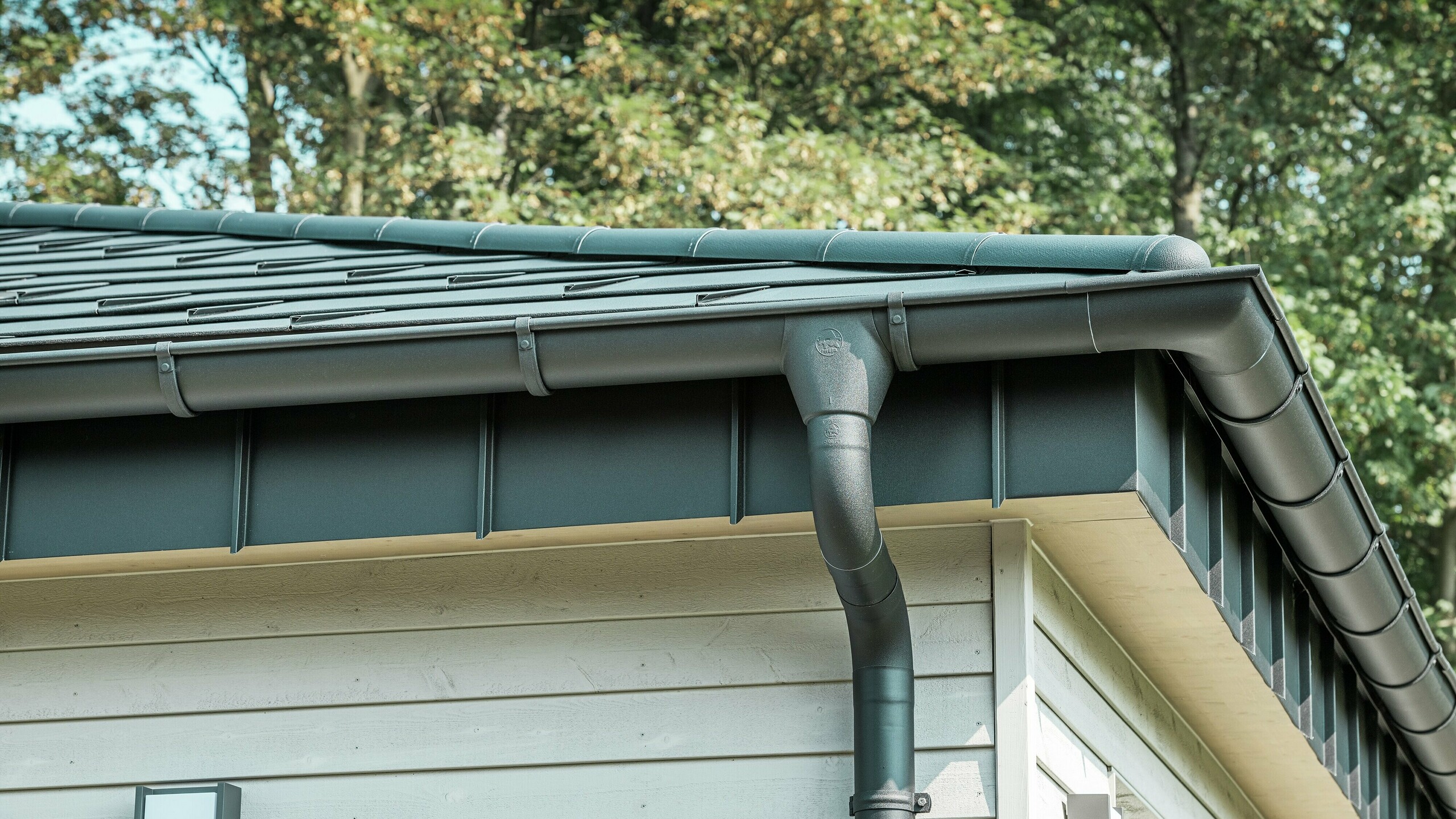 Detaljbild av PREFA Takavvattning på en bungalow i Rommerskirchen. Den högkvalitativa takrännan och avloppsröret i P.10 Svart ger en säker takavvattning vid regn. De hållbara PREFA aluminiumprodukterna kombinerar funktionalitet med modern, elegant design.