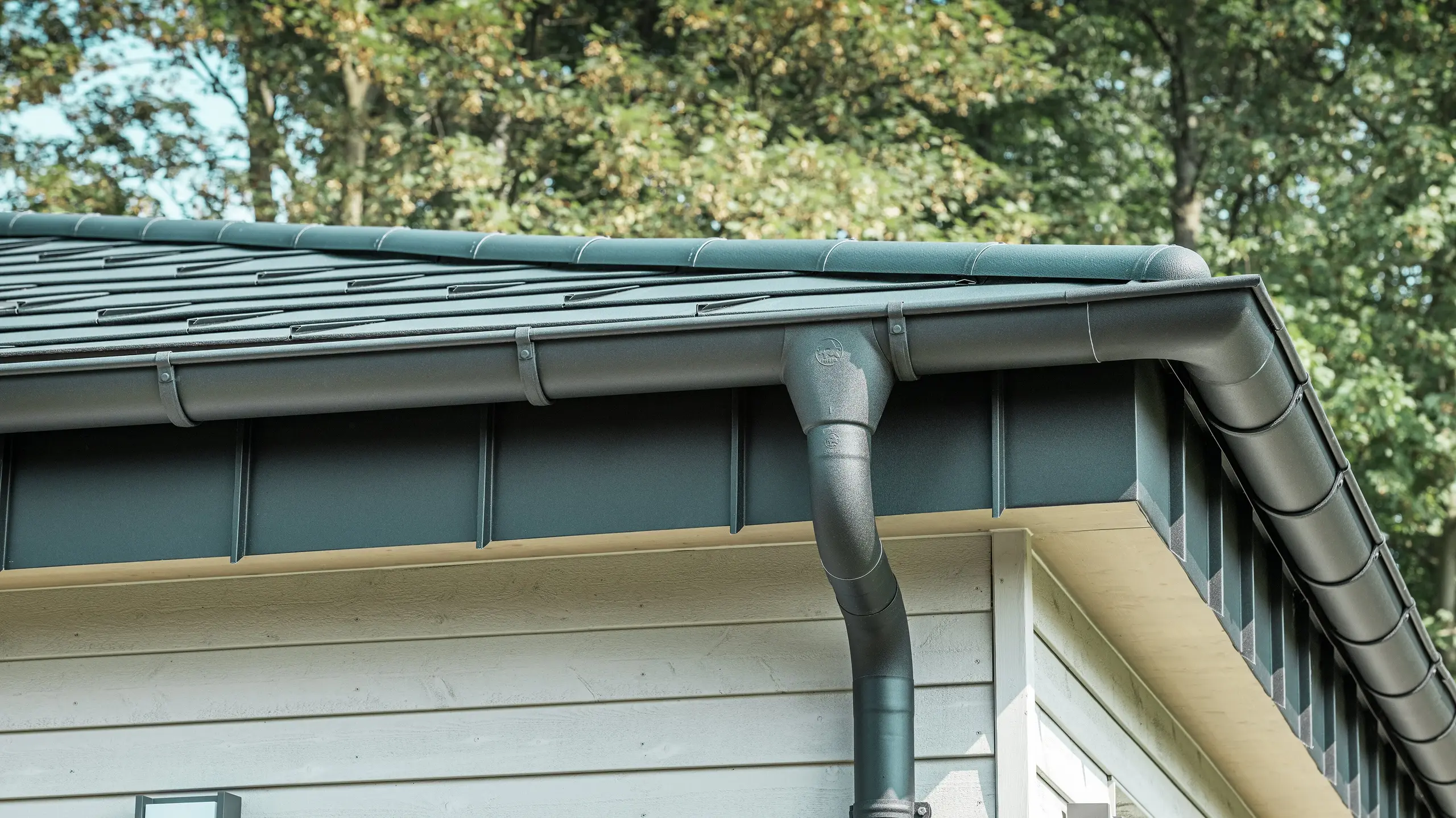 Detaljbild av PREFA Takavvattning på en bungalow i Rommerskirchen. Den högkvalitativa takrännan och avloppsröret i P.10 Svart ger en säker takavvattning vid regn. De hållbara PREFA aluminiumprodukterna kombinerar funktionalitet med modern, elegant design.