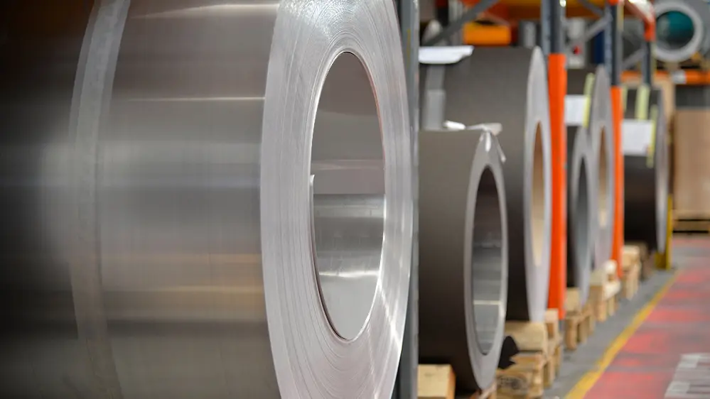 Aluminiumrullar (band) på träpallar, i förgrunden står en valsblank aluminiumrulle och i bakgrunden finns ytterligare band och plåtar av aluminium.