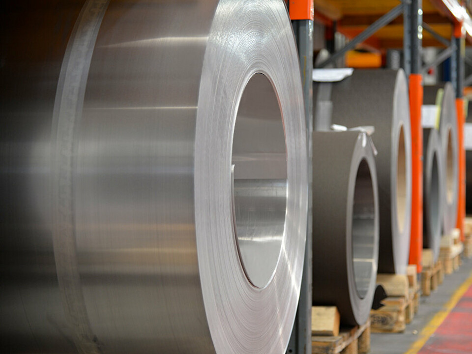 Aluminiumrullar (band) på träpallar, i förgrunden står en valsblank aluminiumrulle och i bakgrunden finns ytterligare band och plåtar av aluminium.