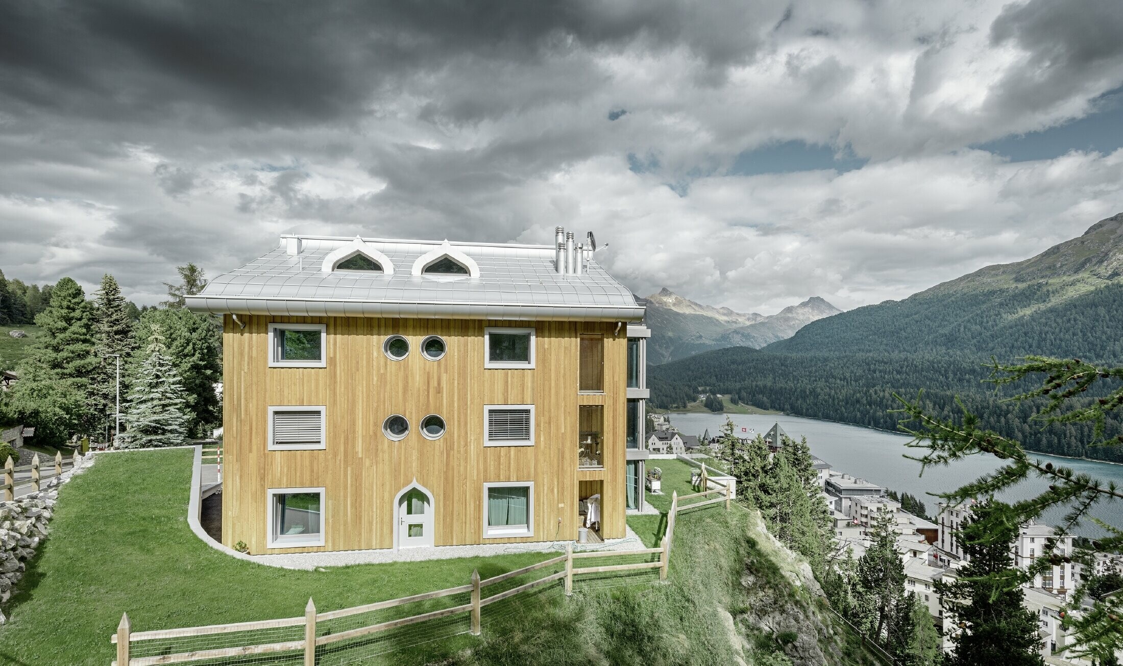 Bostadsbyggnad i St. Moritz med träfasad och aluminiumtak med svängda takskenor i silvermetallic