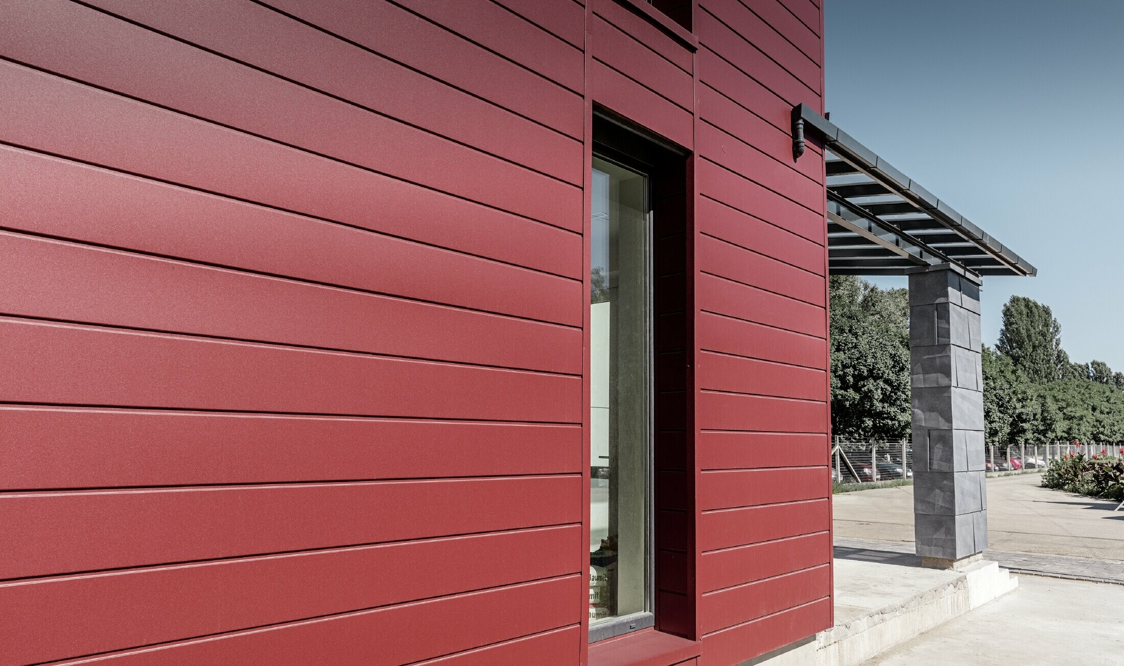Modern kontorsbyggnad med en delad fasad i rött, stengrått och vitt med aluminiumprodukterna fasadpanel, fasadpanel FX.12 och samverkansplatta i aluminium från PREFA